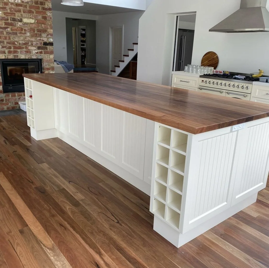 Kitchen island with a wooden butcher block countertop and white cabinetry, located in a modern kitchen with hardwood floors, brick wall, and stainless steel appliances.