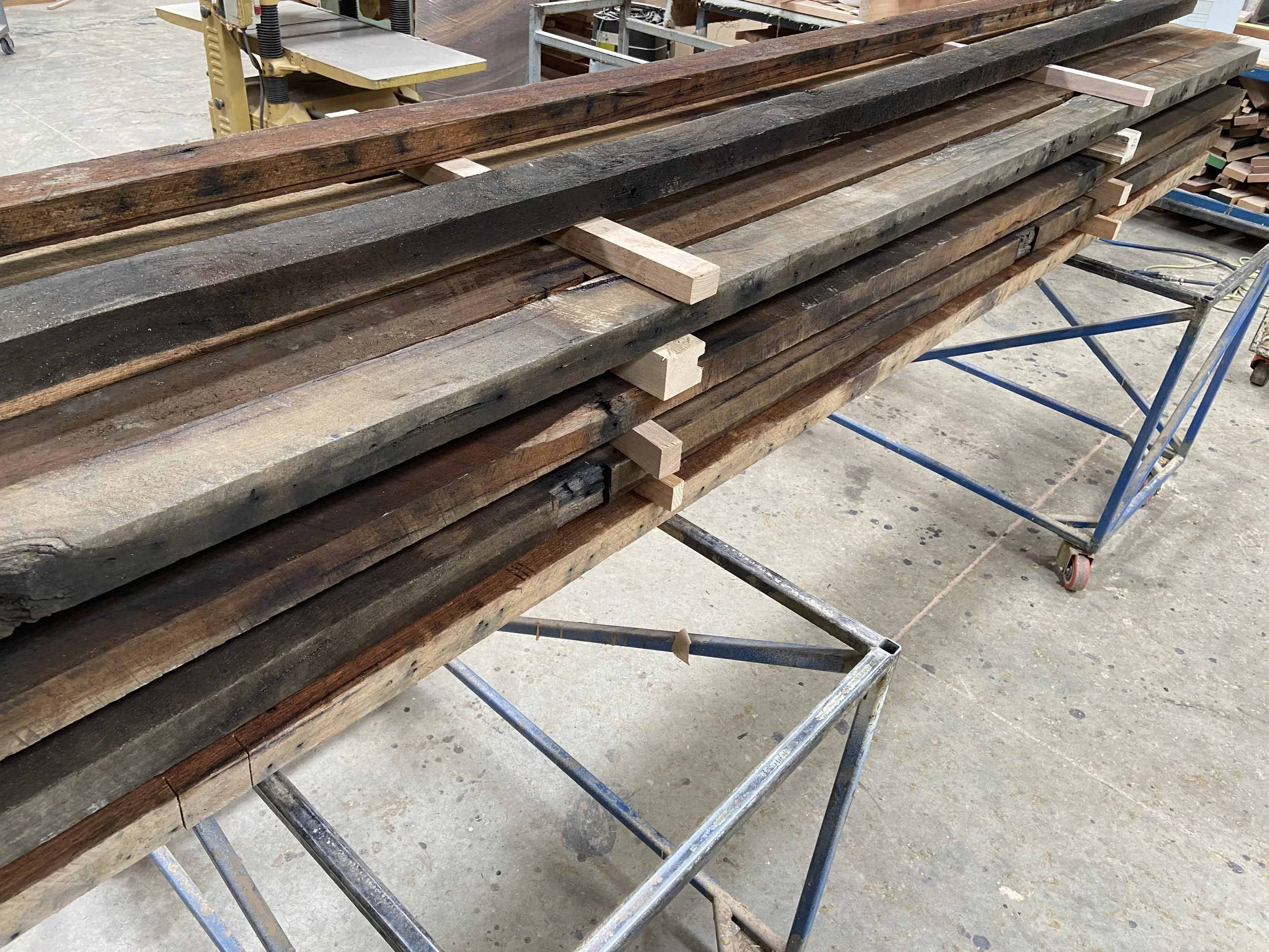 Stack of reclaimed wood and wooden blocks on a metal work table in a woodworking shop.