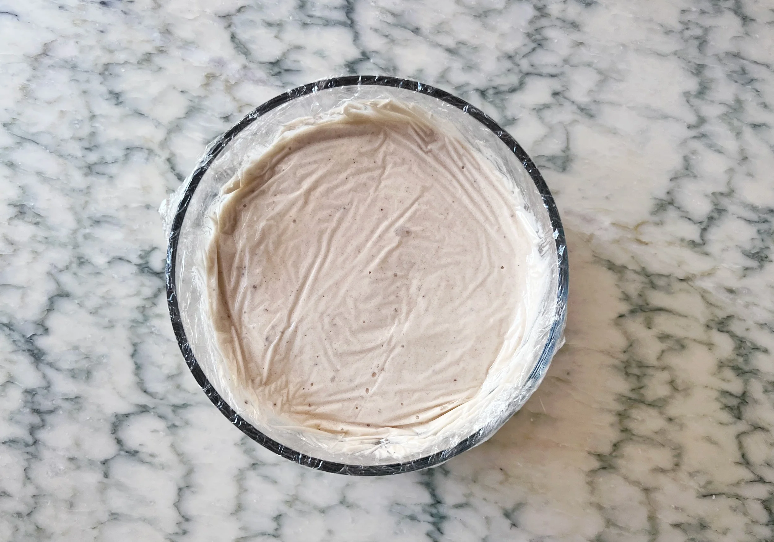 banana honey ice cream in bowl with plastic wrap over it. the plastic wrap is pressed down so there are no air bubbles