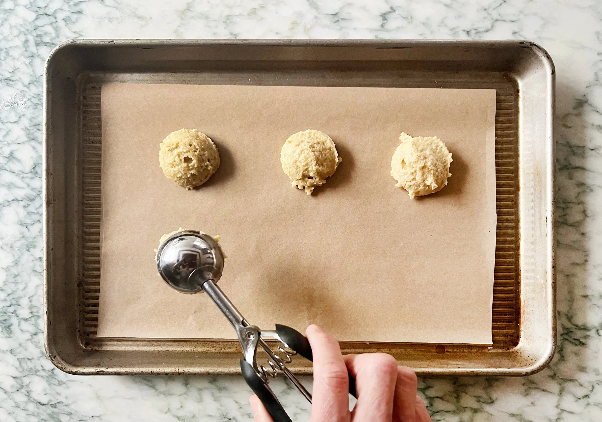 step 2 batter being scooped into ball and placed on a cookie sheet