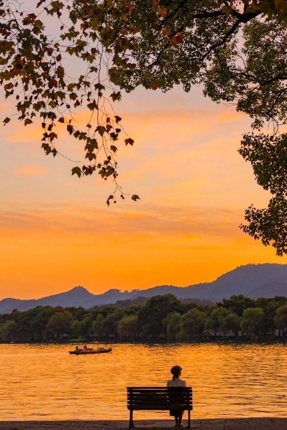 Sunset over a lake with mountains, trees, and a boat in the distance.