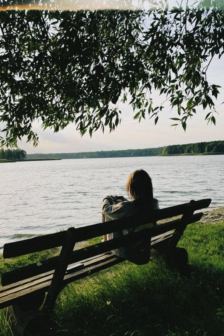 Person sitting on a bench beside a lake, looking out over the water.