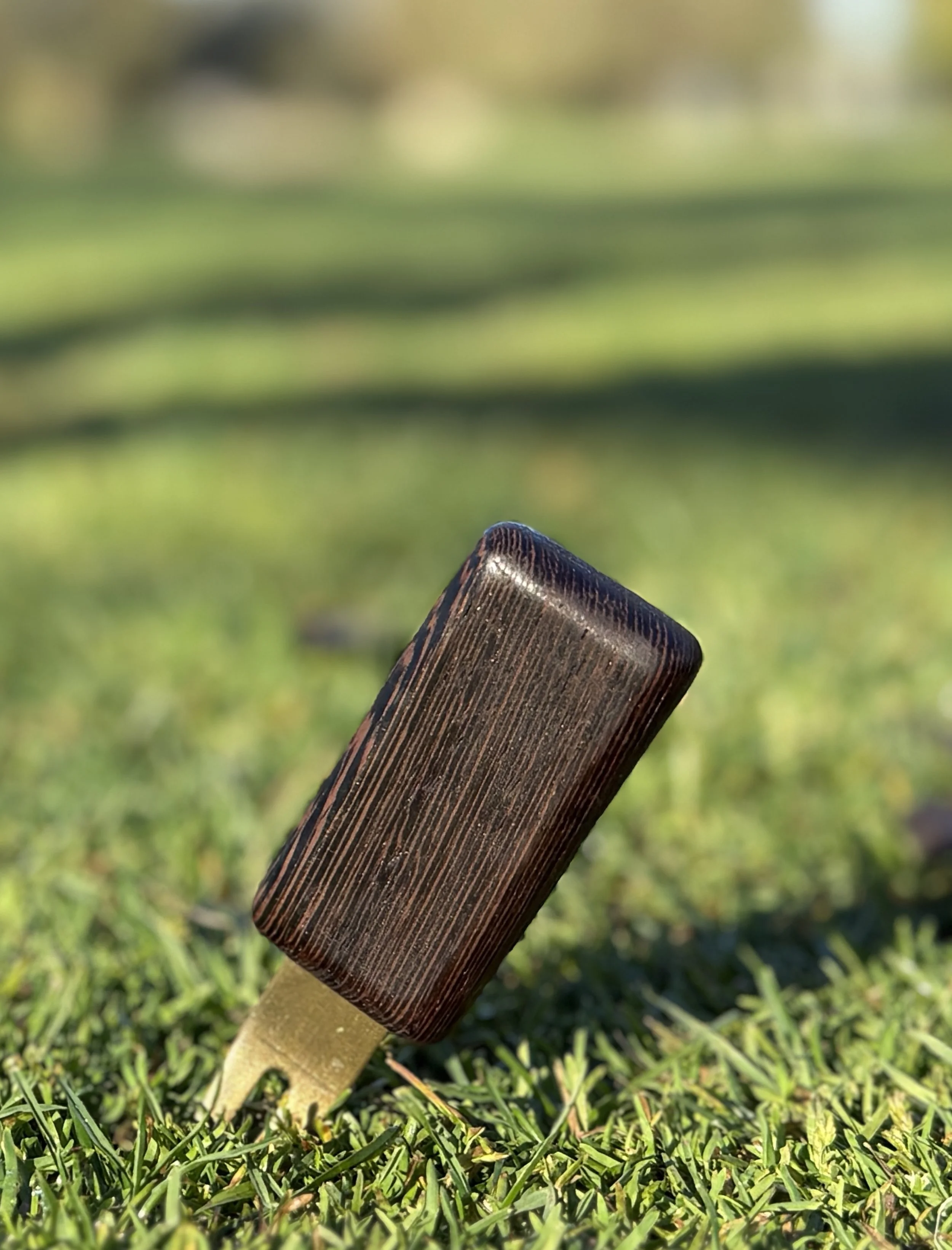 Wenge wood golf divot repair tool by The Divsmith resting in fairway grass on a golf course