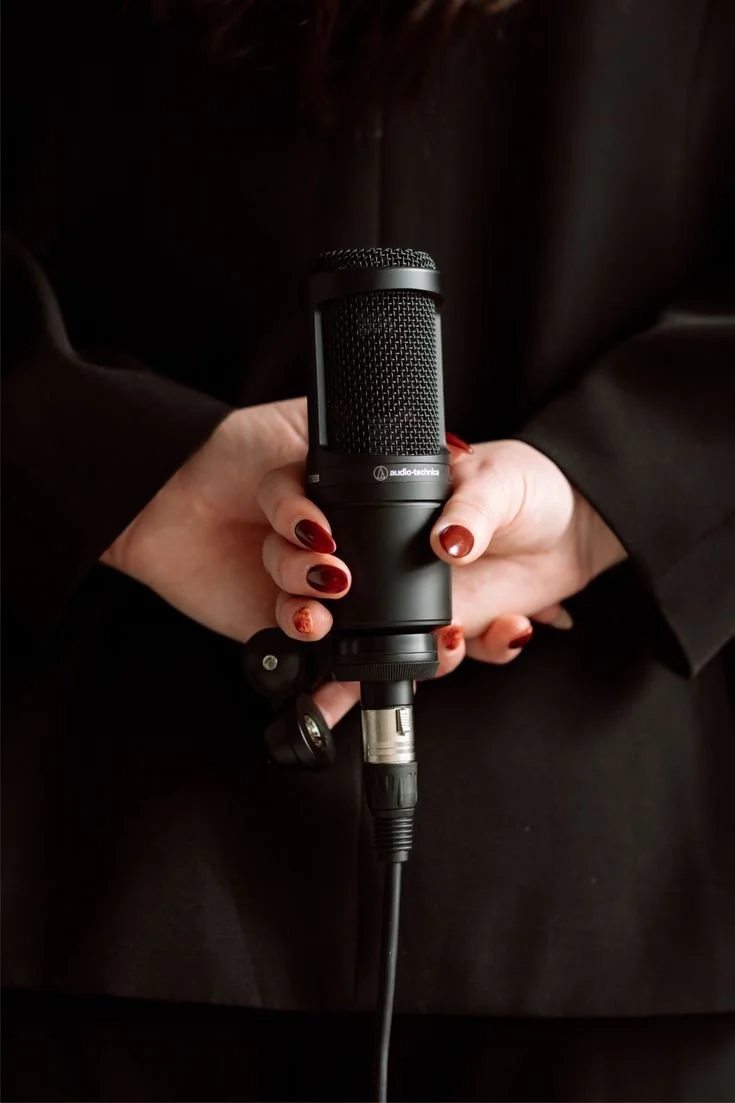 A person holding a black audio-tech microphone with red nails.