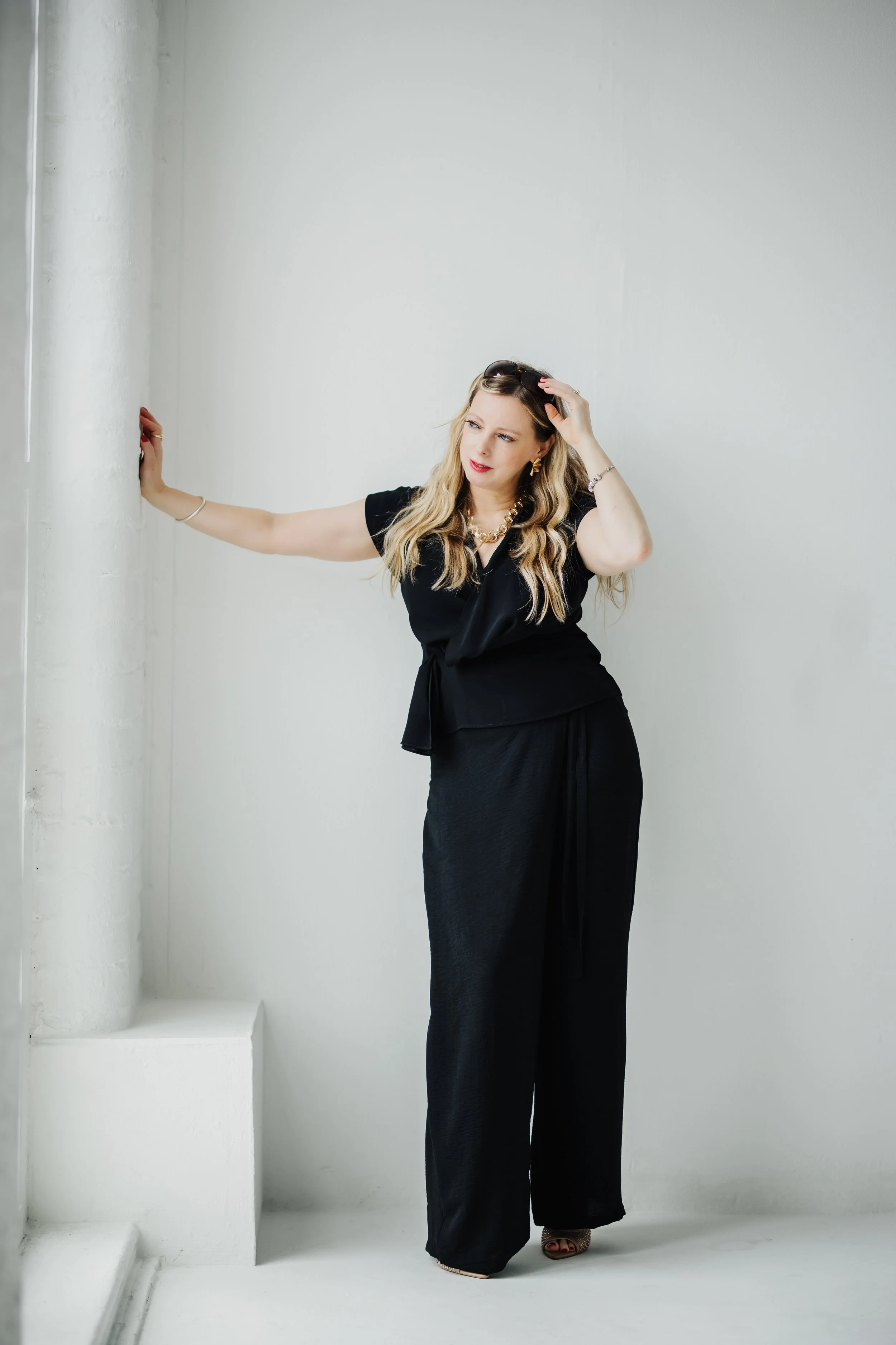 Women in black outfit posing against a white wall.