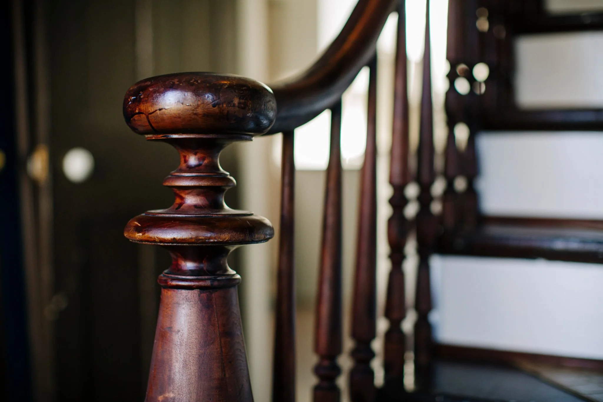 Close-up of a dark polished wooden staircase railing and balusters in a home interior.