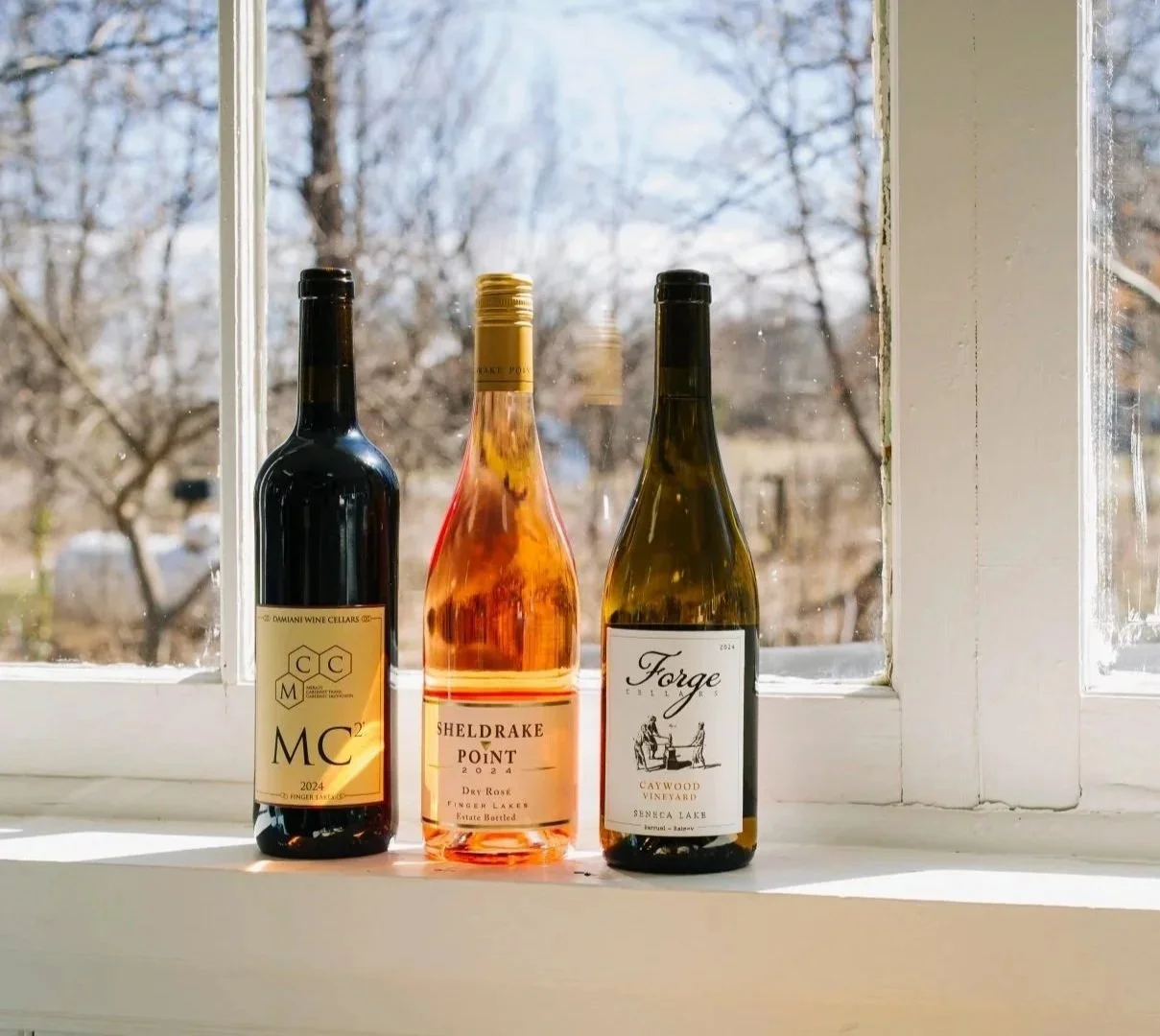 Three bottles of local wine on a windowsill with trees outside in the background.