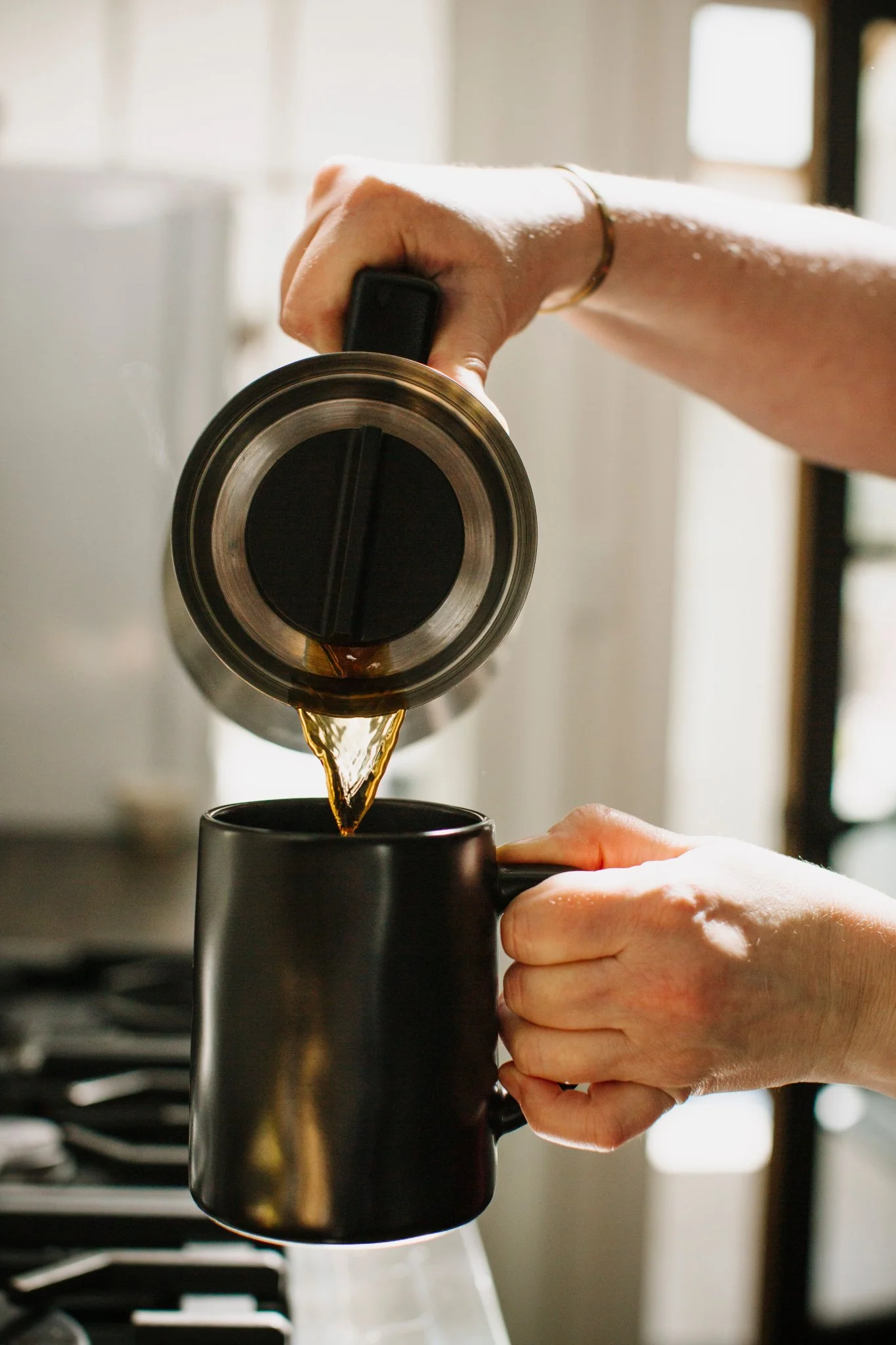 Picture of Jen's hands pouring coffee from a stainless steel thermal carafe into a black mug.