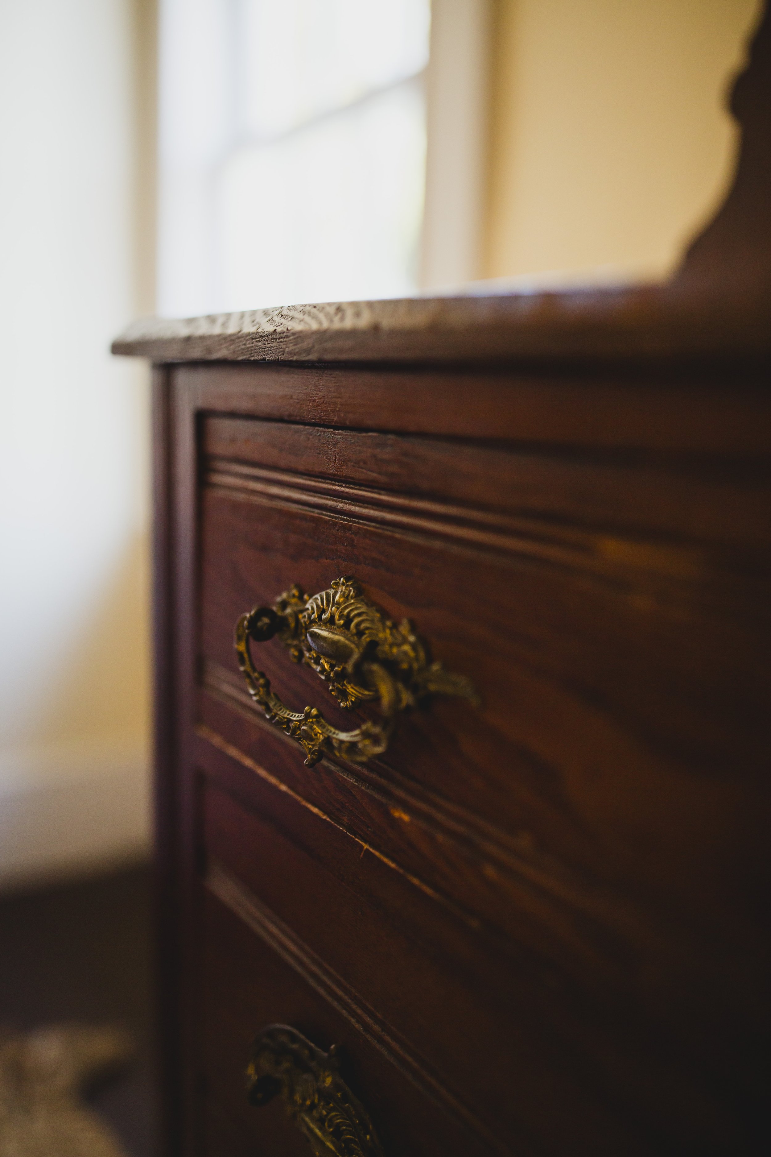 Close-up of a vintage wooden dresser with ornate gold handles and a flat top.