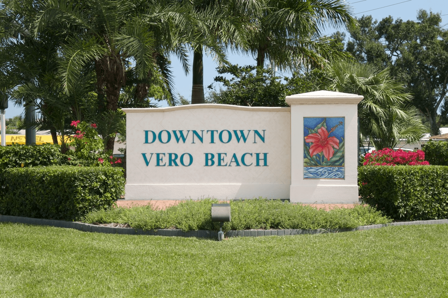 Sign that reads Downtown Vero Beach in front of palm trees and colorful flowers.