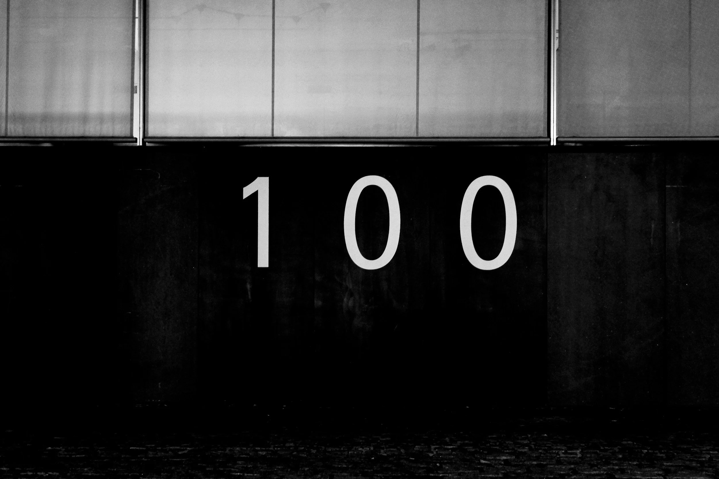 Black wall with the number 100 in white, with reflective windows above.