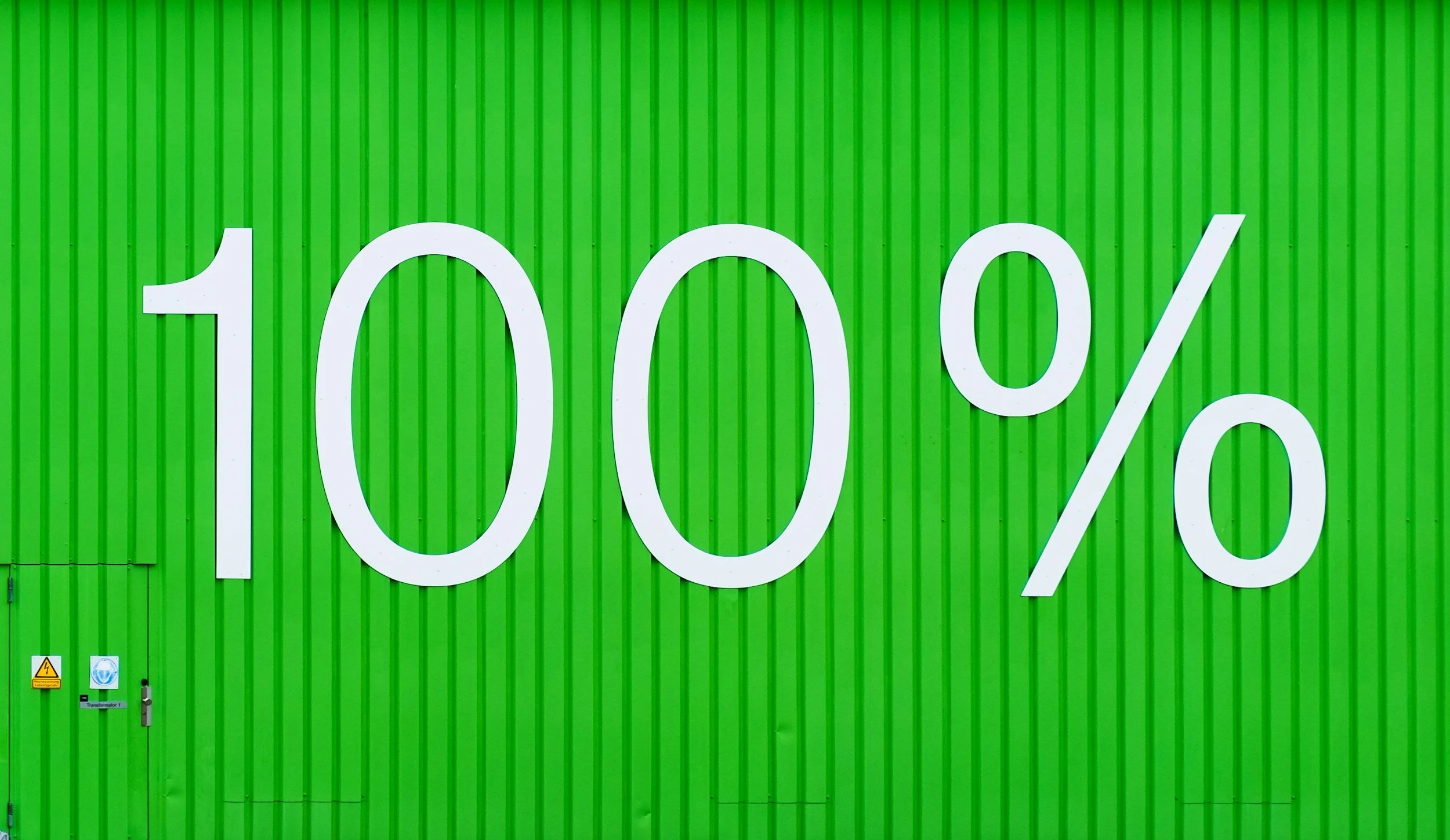 Large white text displaying "100%" on a green corrugated wall.