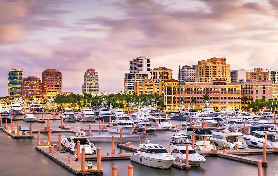 Marina with boats and yachts docked in front of colorful city buildings during sunset