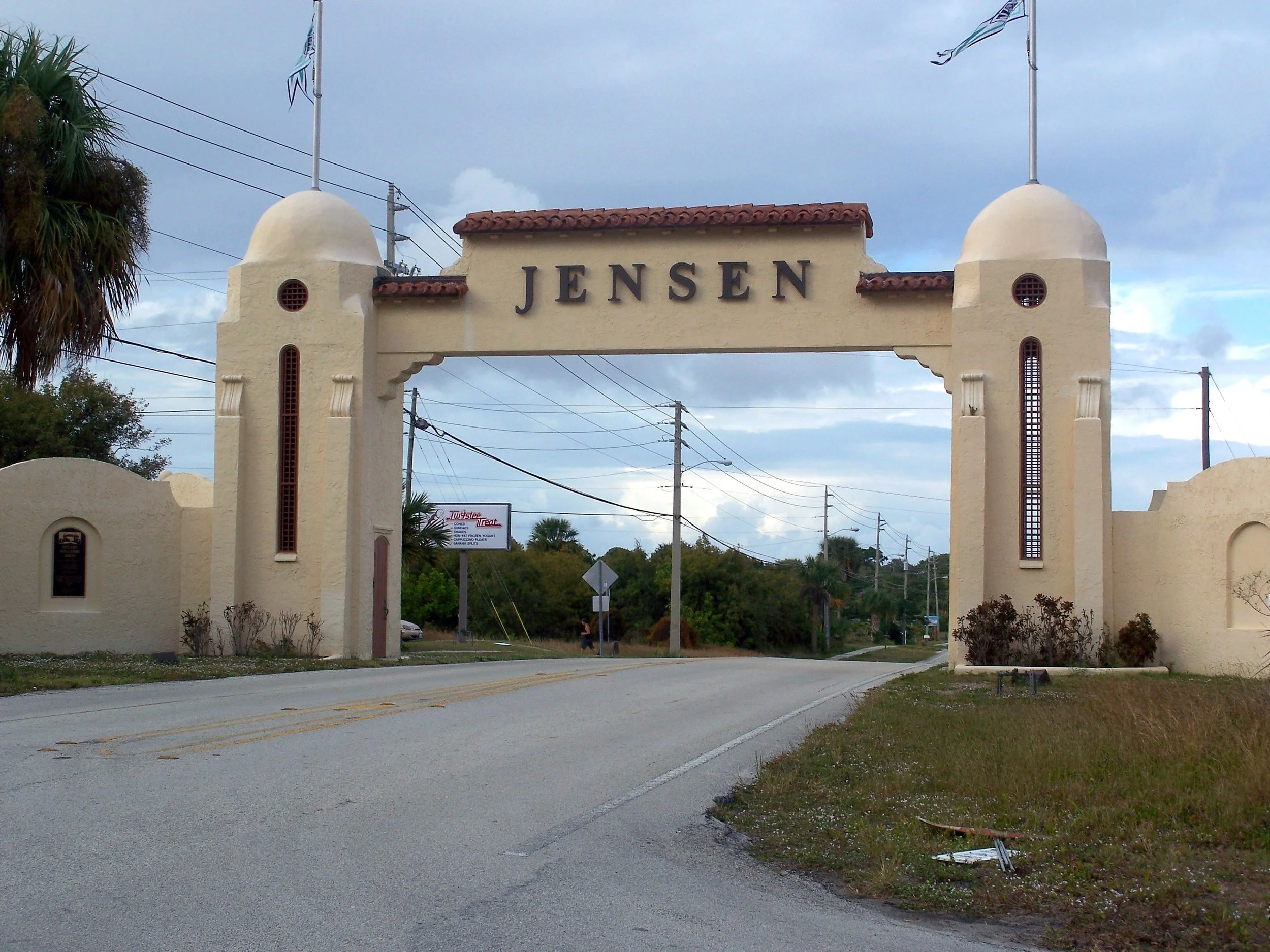 The Jensen entrance archway with the name written on top, palm trees, and utility poles.