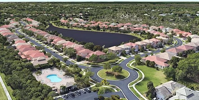Aerial view of a residential neighborhood with houses, a pond, a swimming pool, and greenery.