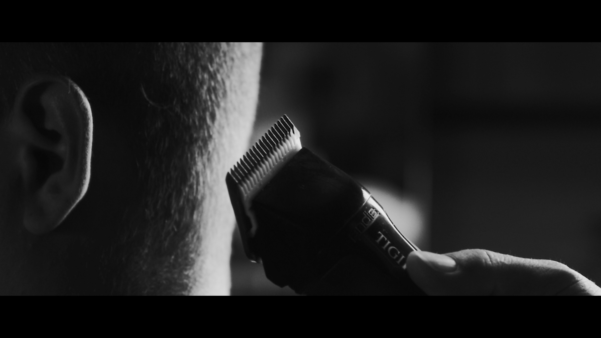 A person is getting a haircut with an electric hair clipper close to the side of their head in a black and white photograph.