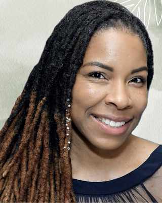 A smiling woman with long, textured dreadlocks wearing earrings and a dark top.