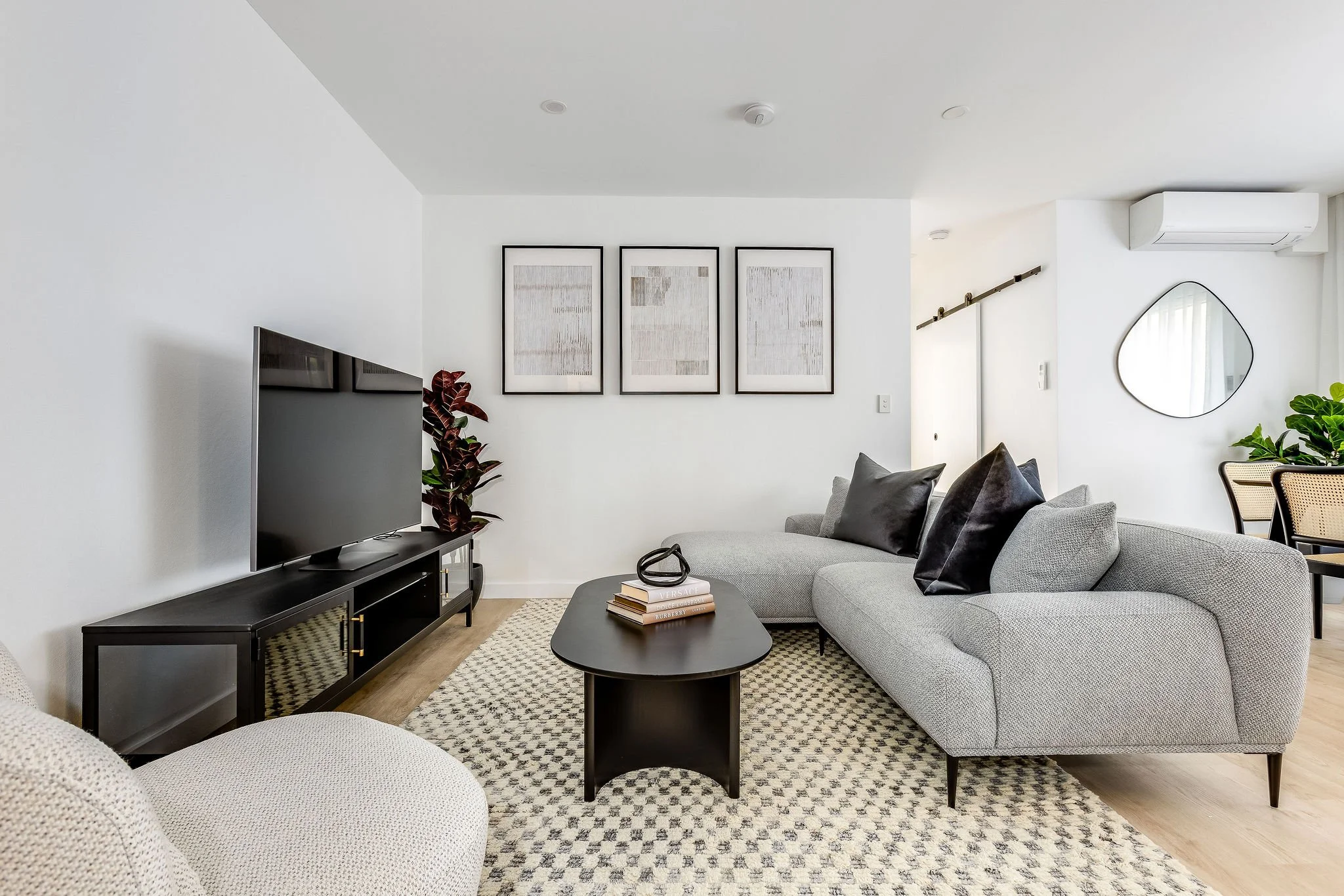 Modern living room with gray sectional sofa, black coffee table, flat-screen TV, framed artwork, and a decorative mirror, with neutral colours and modern decor.