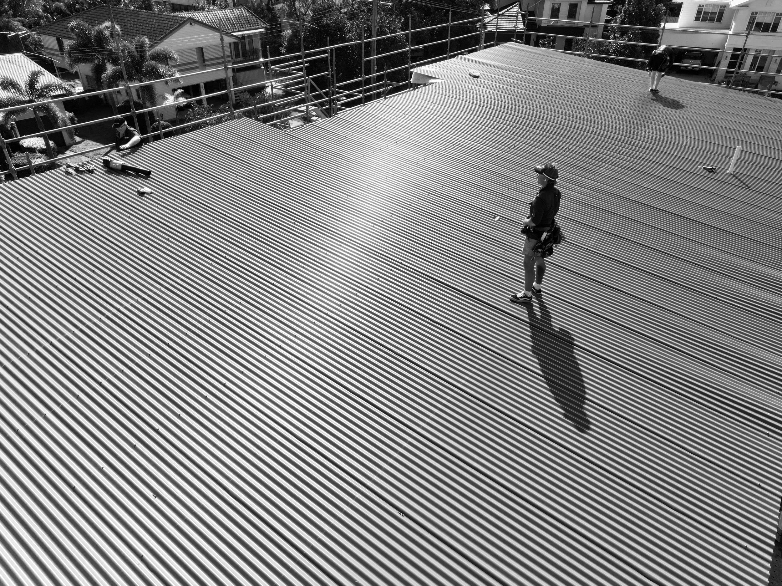 People working on a corrugated metal roof with scaffolding around it, over a residential neighborhood.