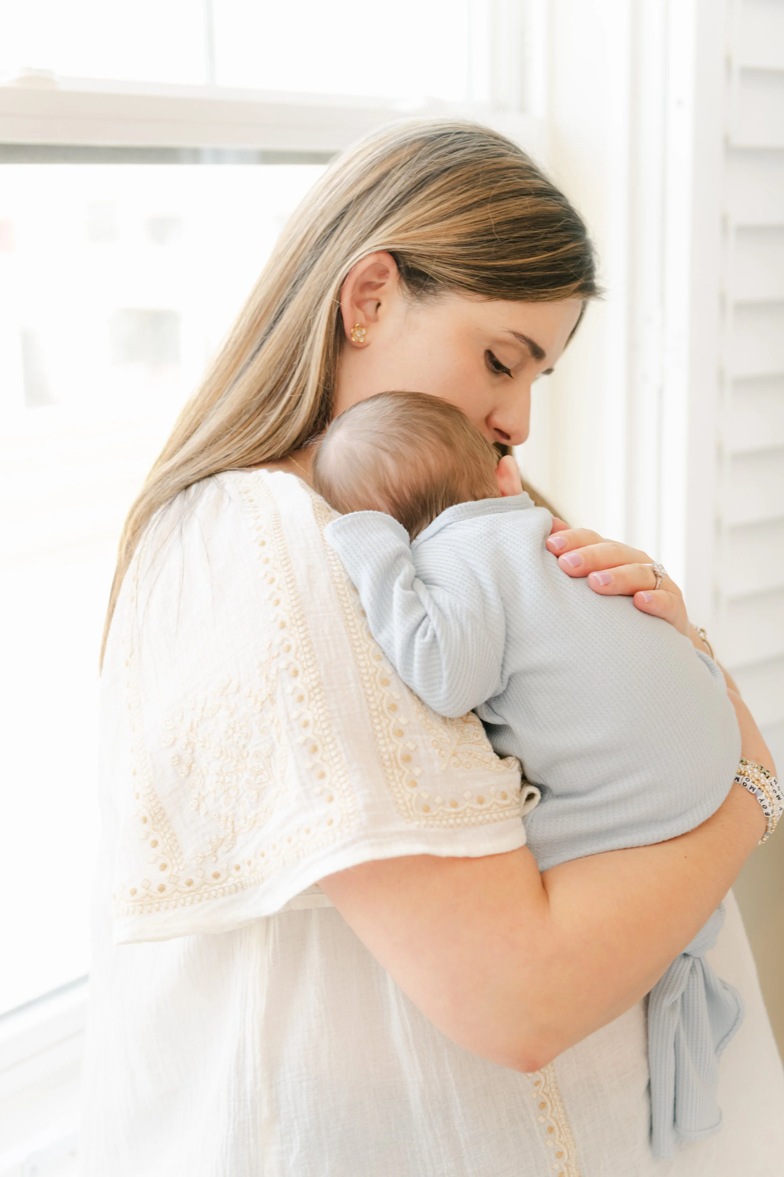 A woman holding a sleeping baby close, showing affection in a bright room.