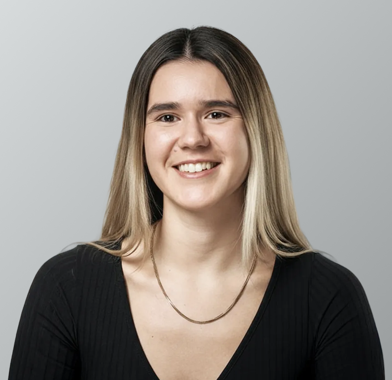 A young woman with shoulder-length brown hair, smiling, wearing a black top and a thin gold necklace, against a plain gray background.