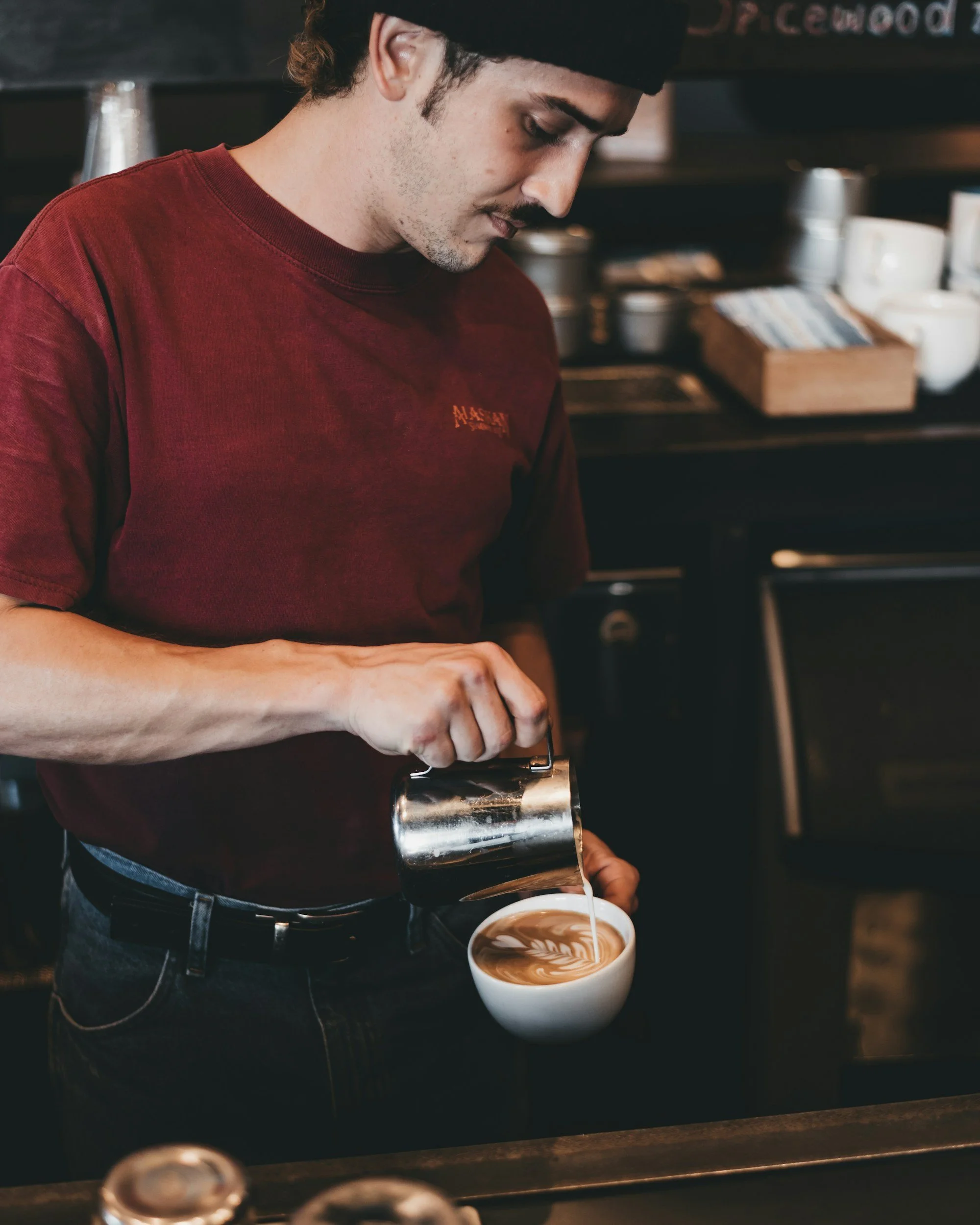 Barista pouring steamed milk into a cup of coffee, creating latte art at a coffee shop.