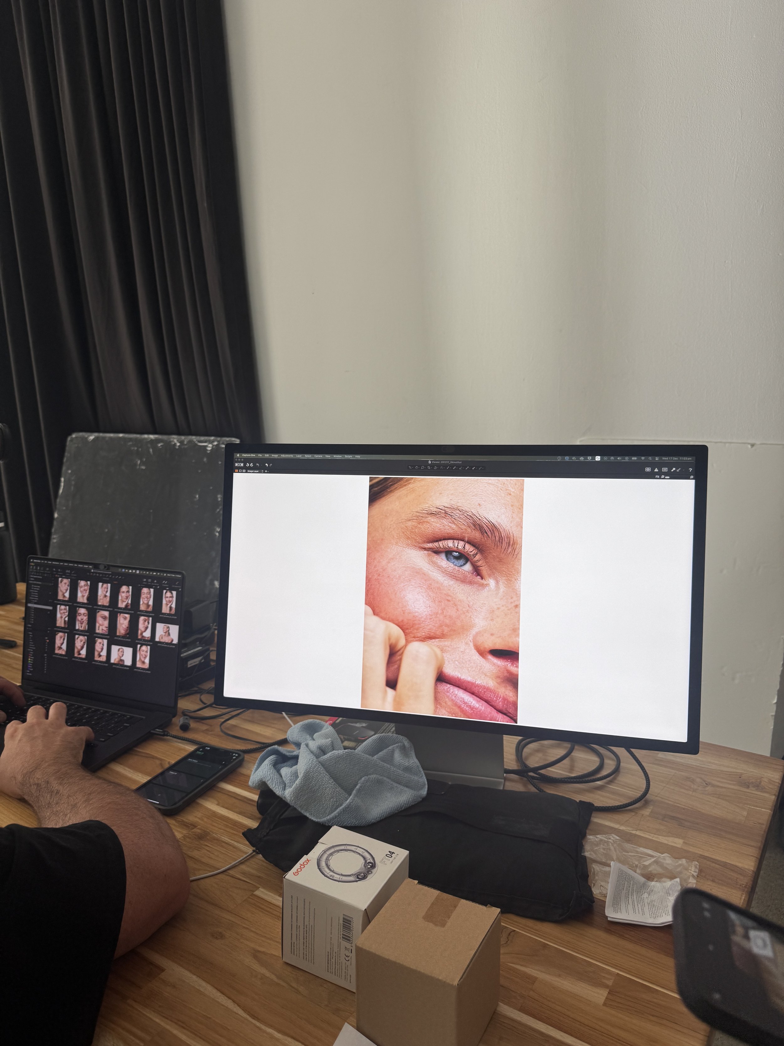 A computer monitor displaying a close-up image of a person's face with a focus on the eye, with a smaller monitor showing a gallery of similar images on the left. The scene appears to be a workspace or studio for photo editing or digital art.