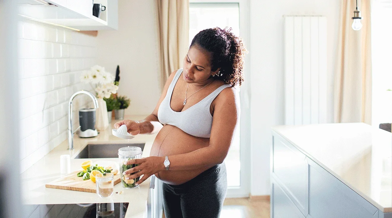 Pregnant woman preparing a drink in a bright kitchen.