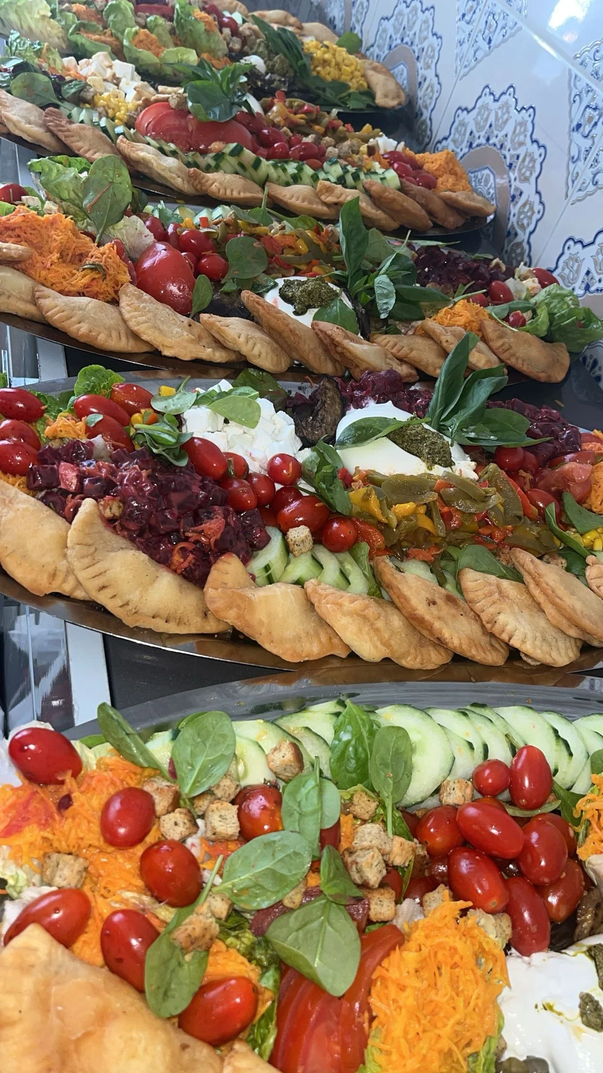 plateaux de salades avec des tomates cerises, des feuilles de basilic, du concombre, du fromage, ainsi que des tartes salées garnies de légumes, de viande et de fromage.