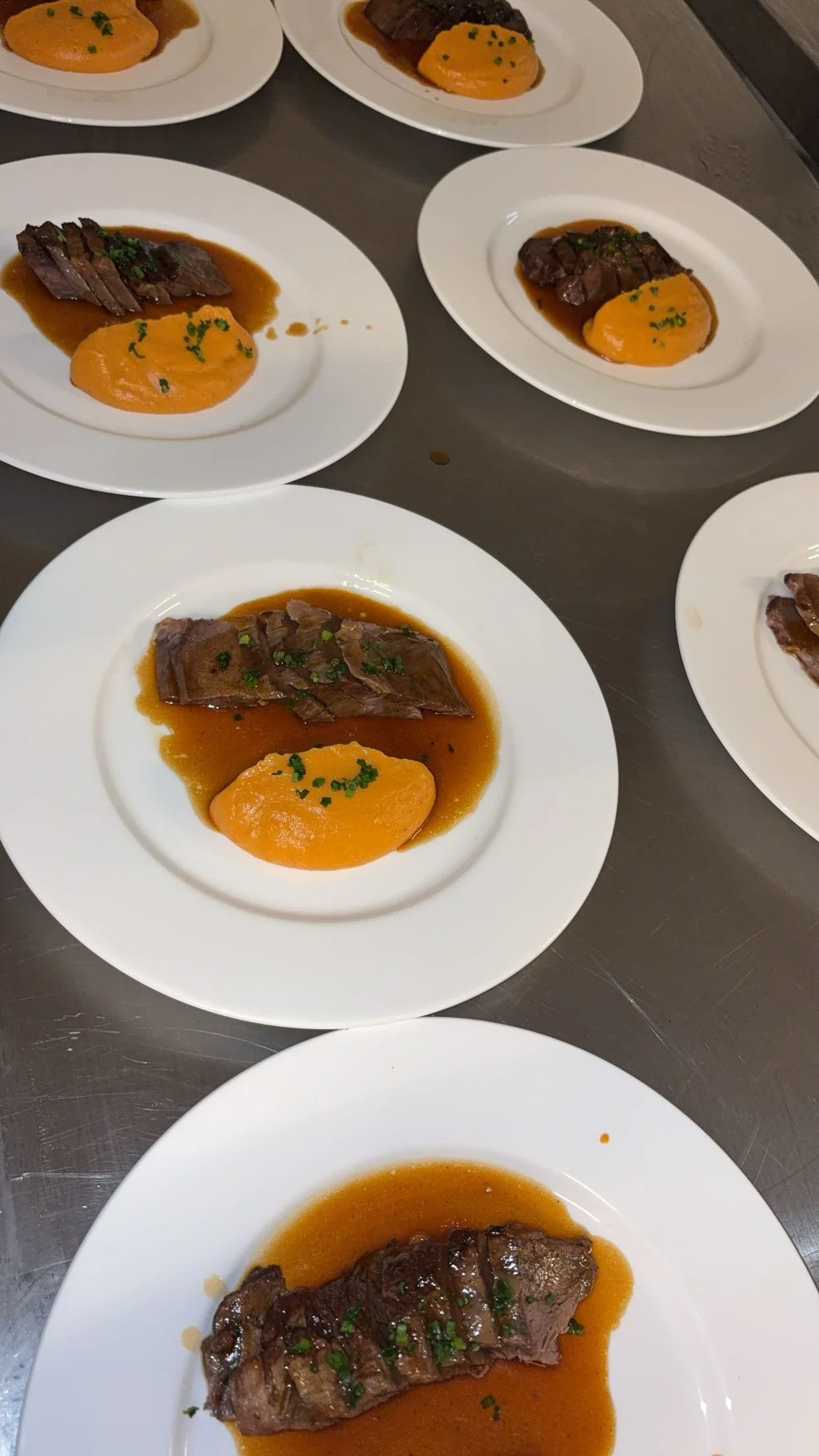 Assiettes avec des morceaux de viande, une purée orange et une sauce brune, garnies de ciboulette