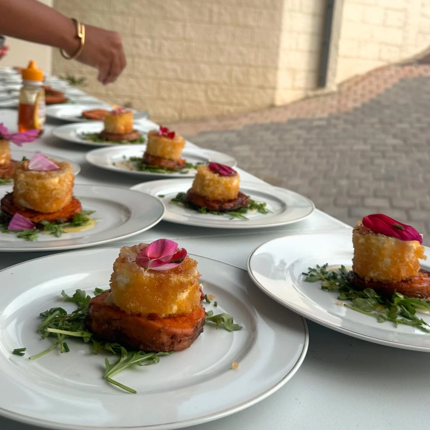 Assiettes avec un muffin de maïs doré, placé sur une tranche de viande, décoré de pétales de fleurs roses, sur un lit de verdure