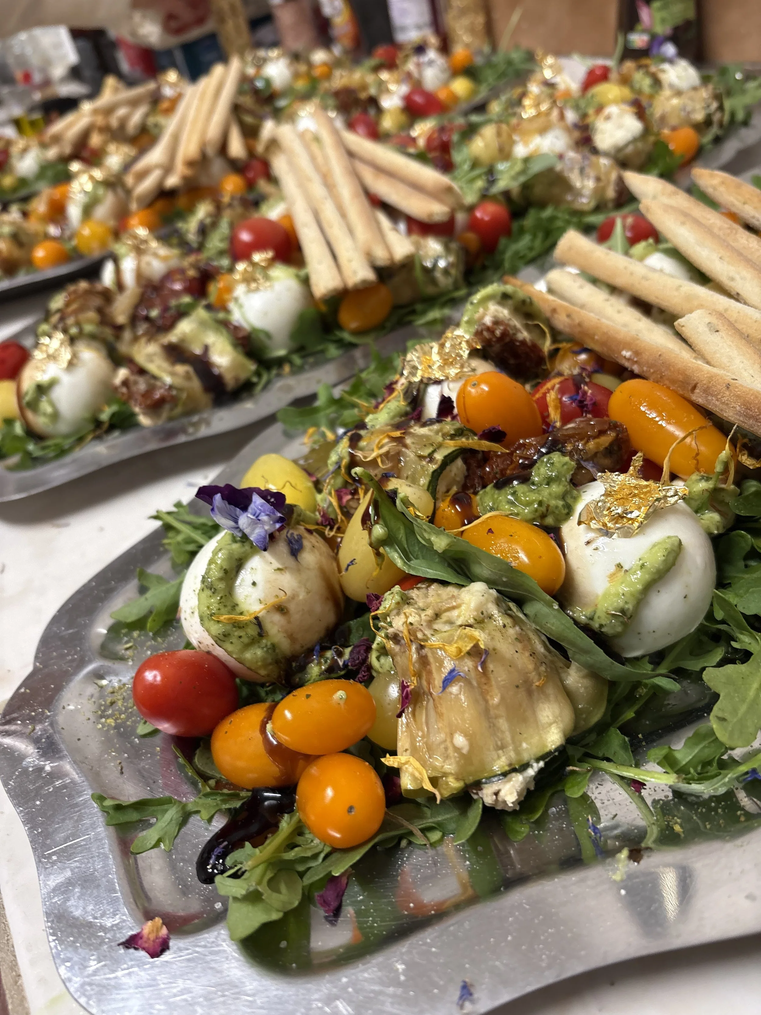 Plate de salade avec des tomates cerises, des billes de mozzarella, des feuilles de basilic, des fleurs comestibles, et des tranches de pain, décorée avec de l'huile d'olive.
