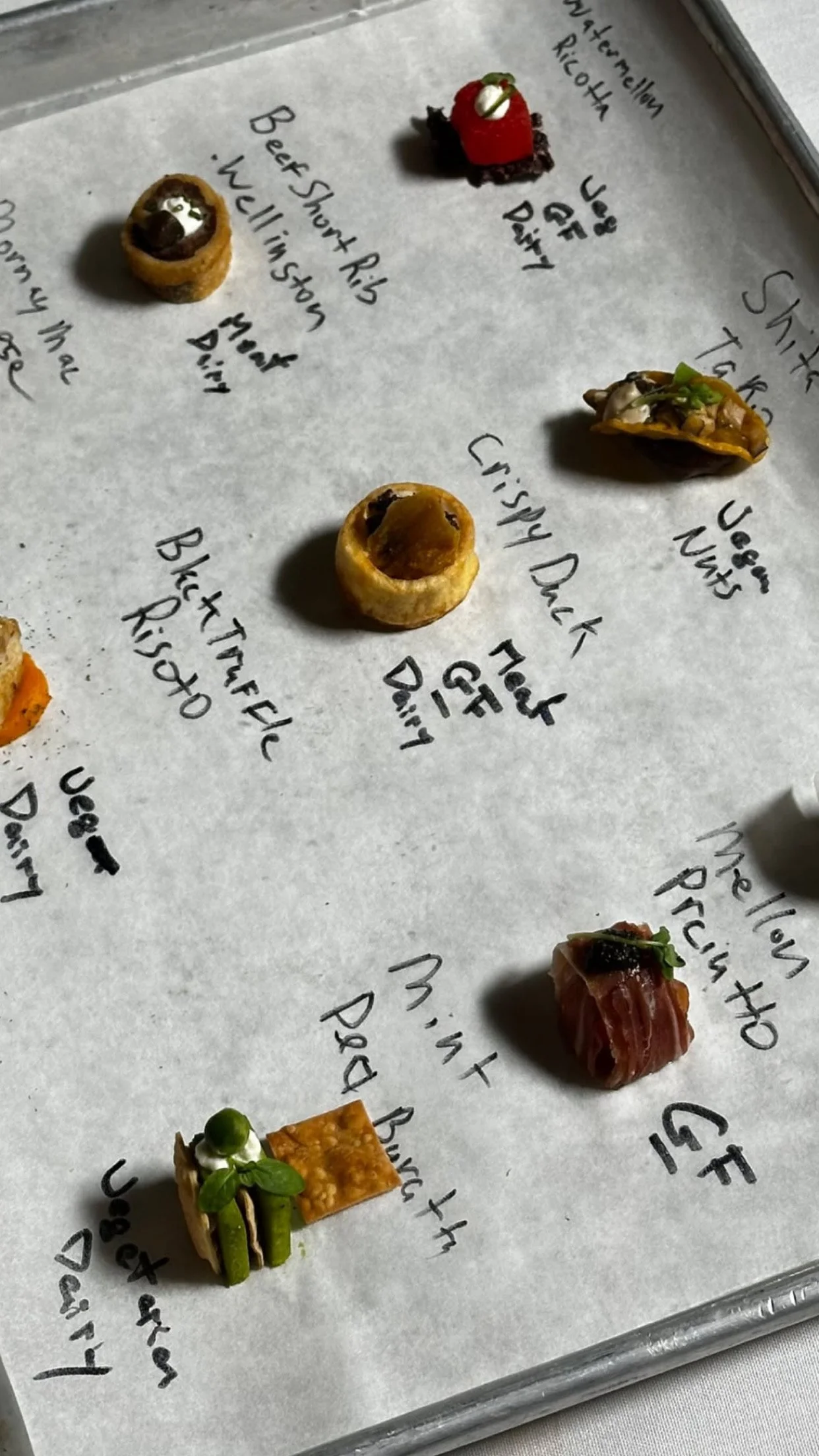 Mini tartelettes et amuse-bouches avec garnitures diverses, accompagnés de leur nom écrit à la main sur un papier