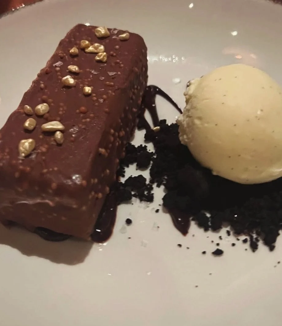 Un dessert composé d'une bûche au chocolat garnie de perles de chocolat, une boule de glace à la vanille, du chocolat en miettes et de la sauce au chocolat.