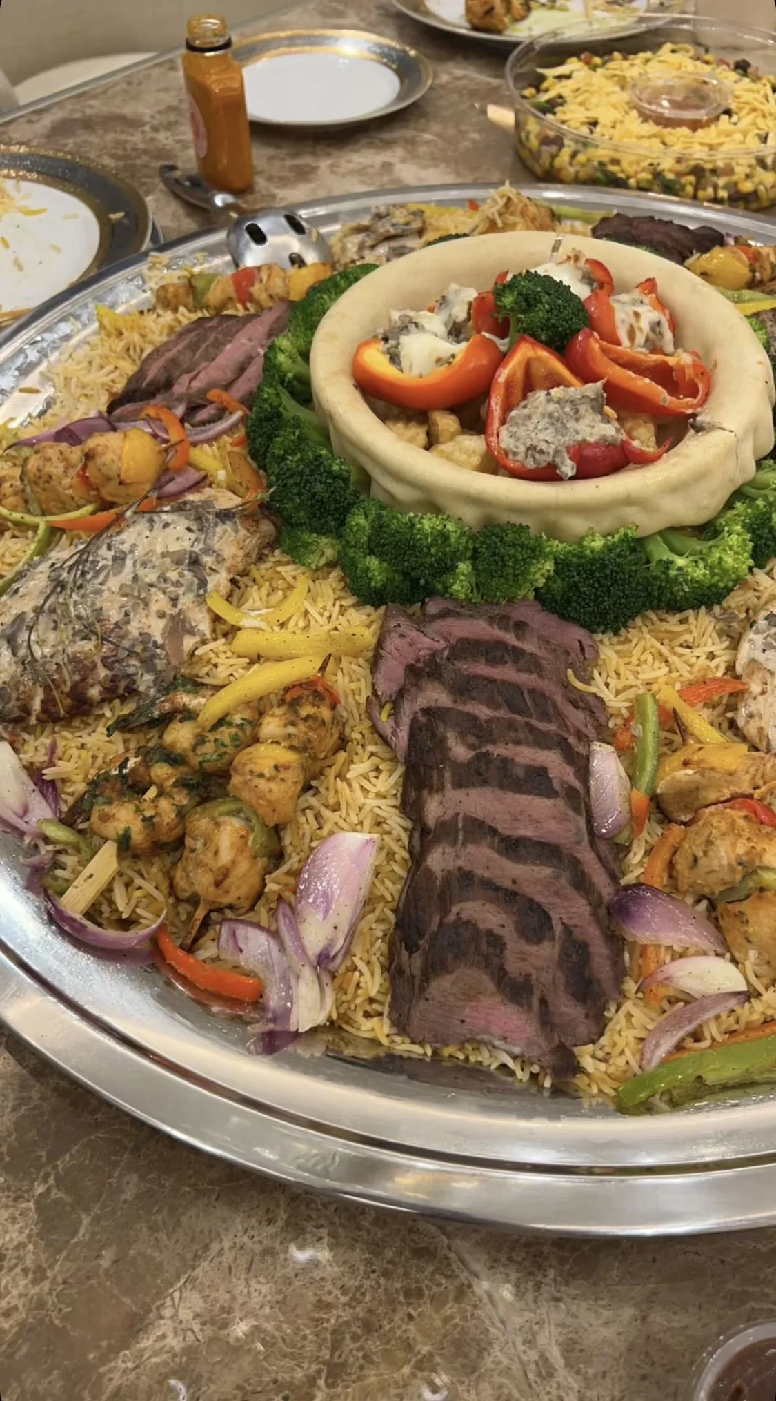 Plate de riz avec diverses viandes, légumes, et un centre avec un fond de pâte et des poivrons, servie avec une garniture de brocoli.