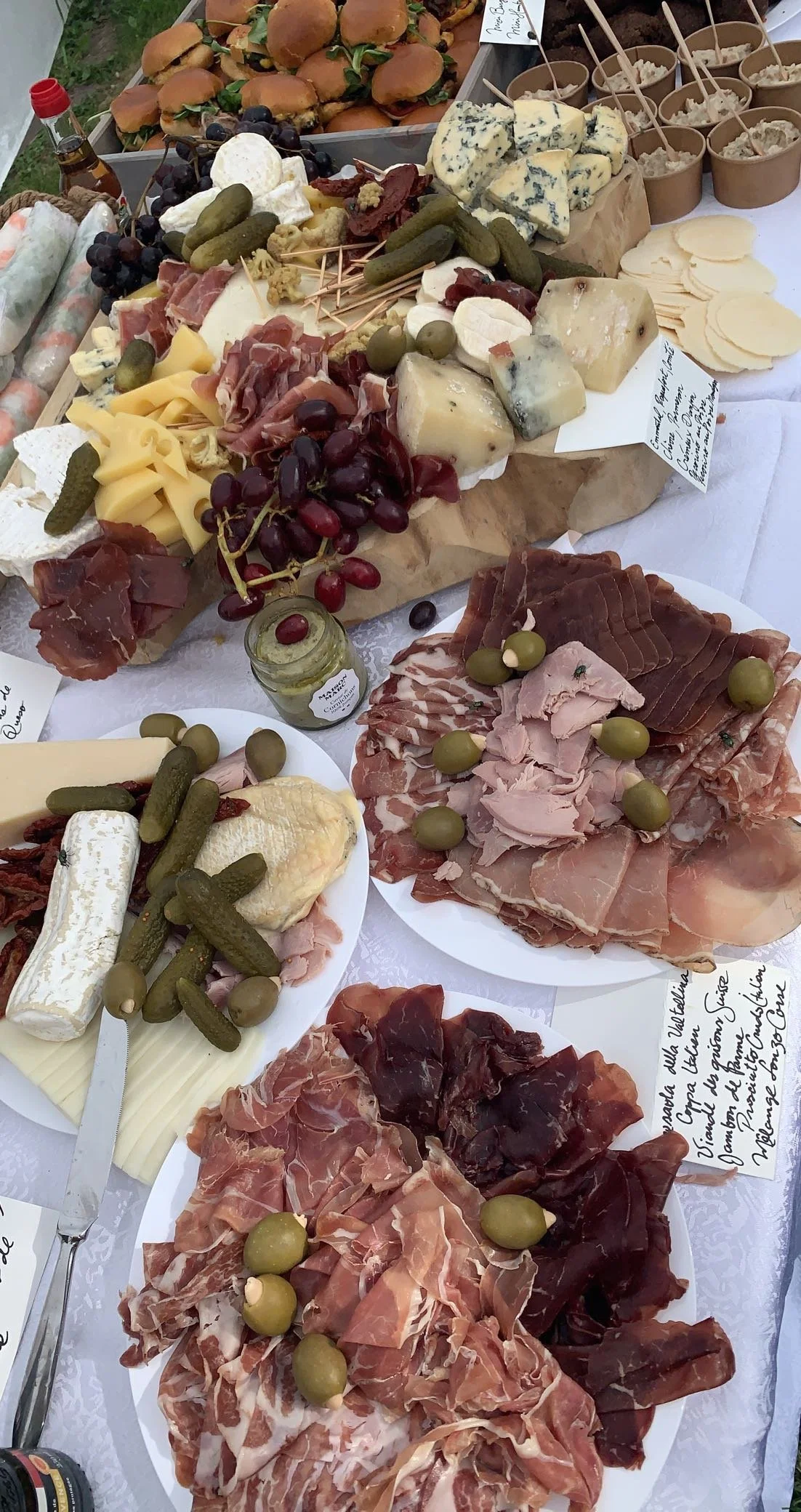 Plat de fromages, charcuterie, raisins, cornichons et petits sandwiches sur une table de buffet.