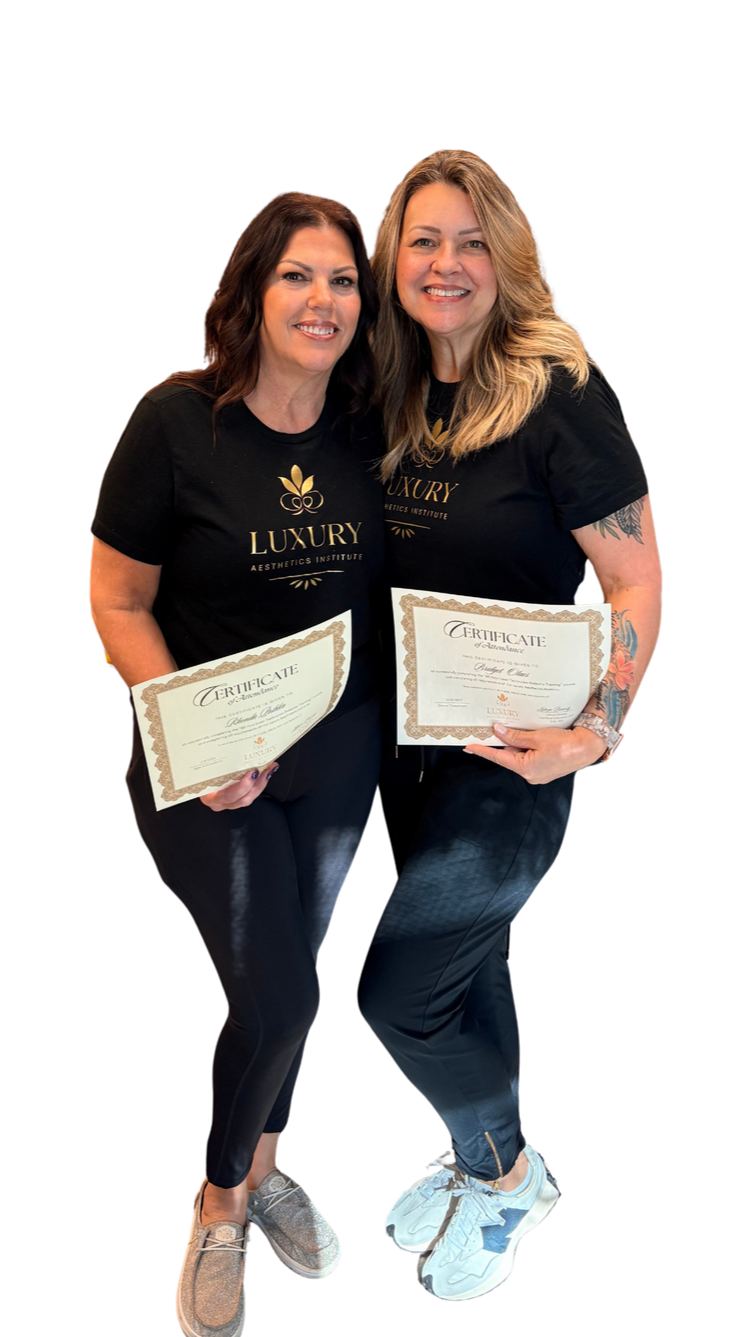 Two women standing together, each holding a certificate, wearing black T-shirts with 'LUXURY AESTHETICS INSTITUTE' logo, smiling, and posing for a photo.