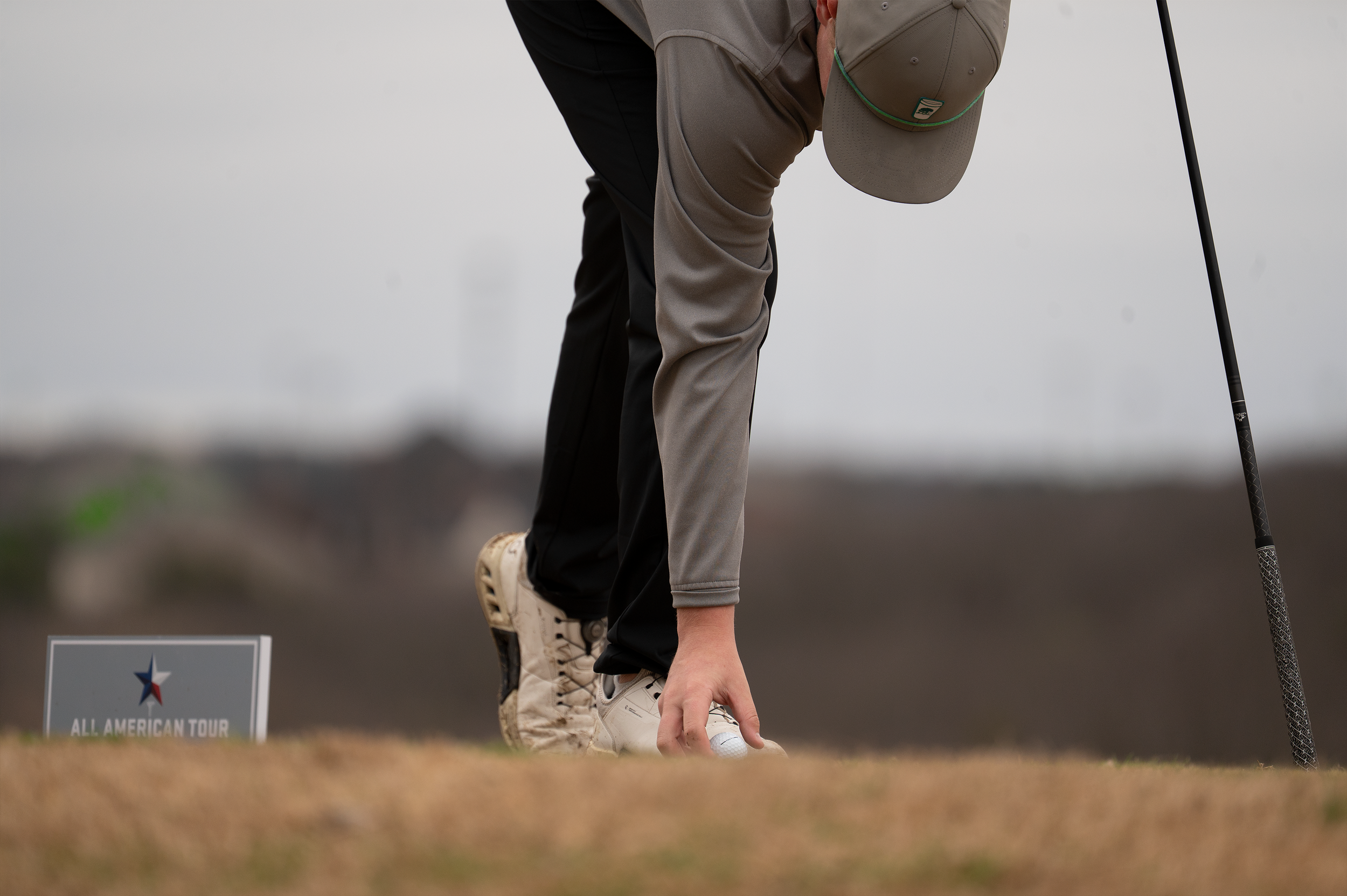 A golfer is placing a golf ball on the ground on a golf course, with a club in hand, during a tournament.