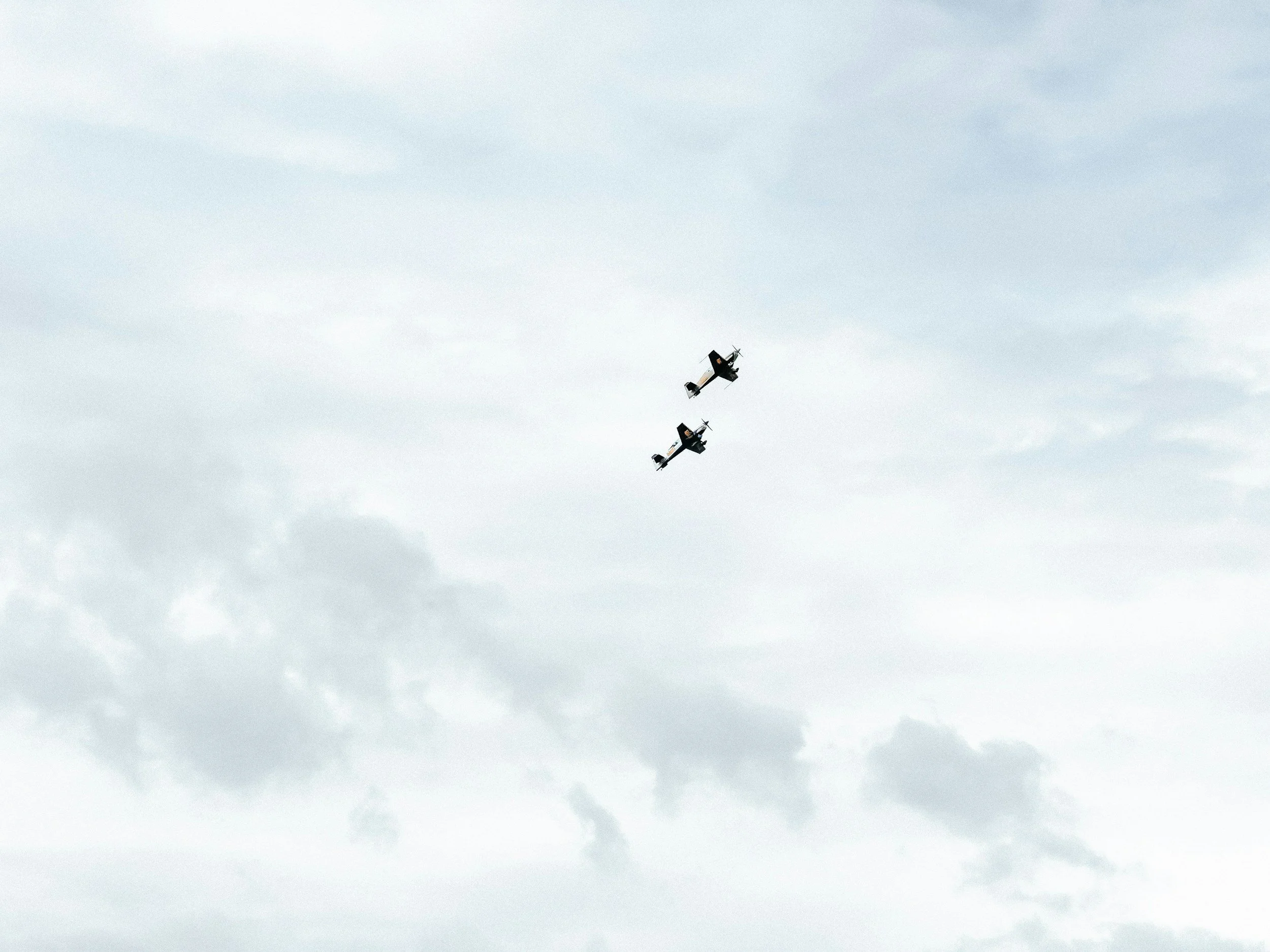 Two small propeller airplanes flying in formation in the cloudy sky.