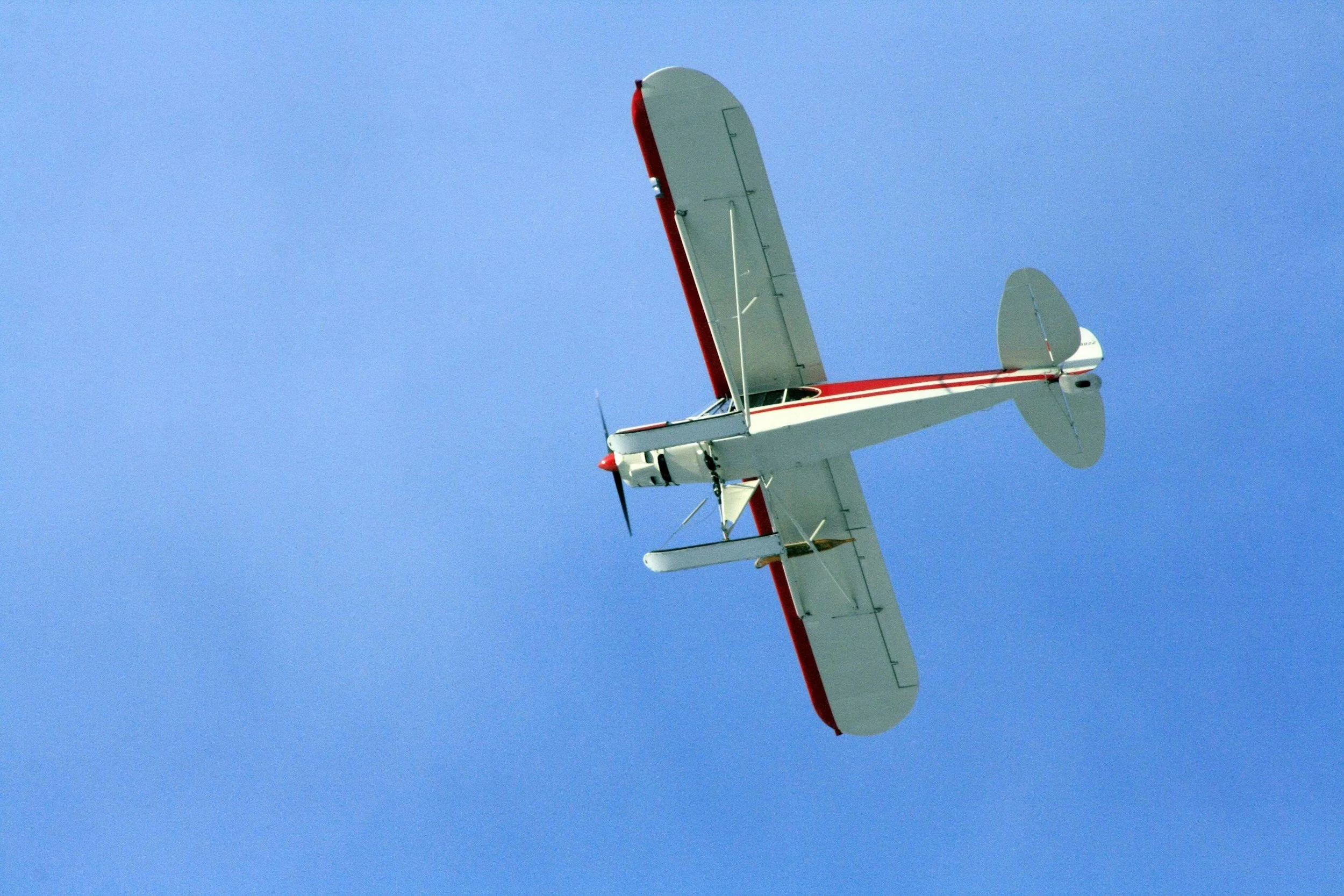 A small white airplane with red accents flying in a blue sky.
