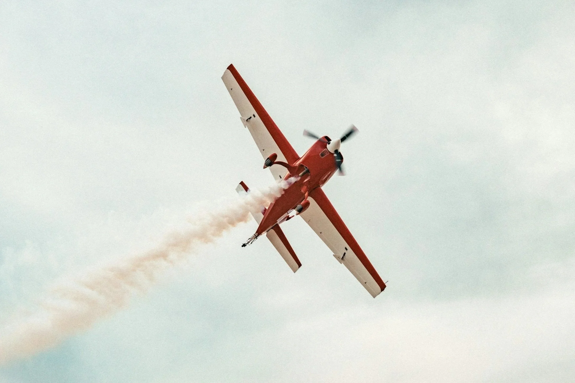 Red and white stunt aircraft performing a dive with smoke trail in the sky.