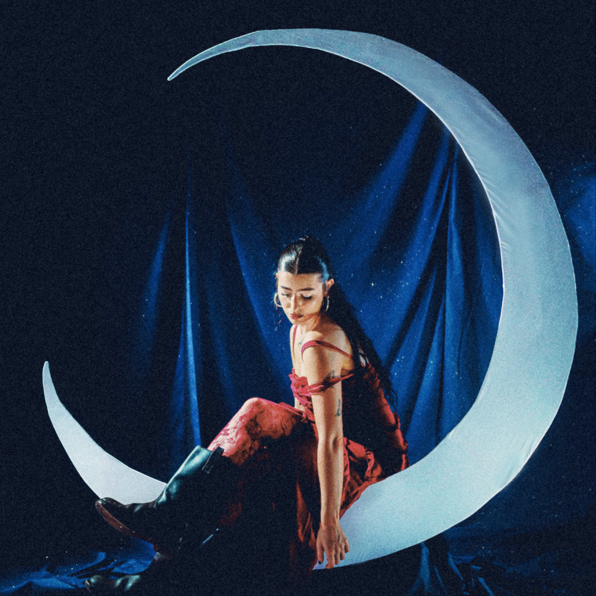 A woman sitting on a crescent moon prop against a night sky backdrop with blue lights.