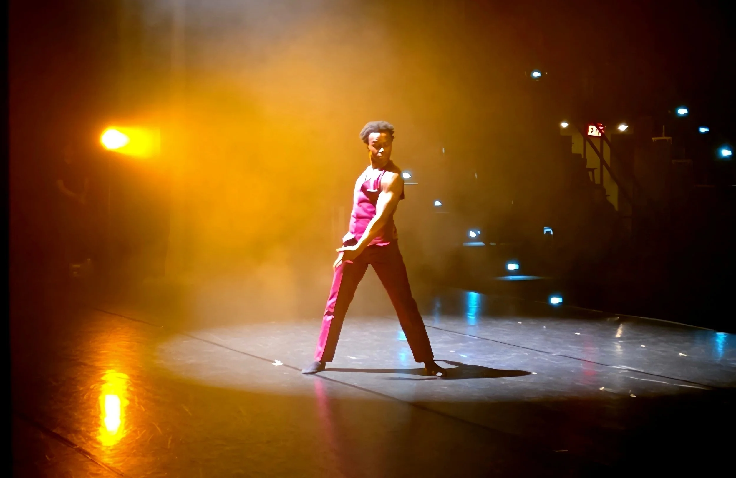 A dancer in a pink costume performing on stage with dramatic yellow and blue lighting.