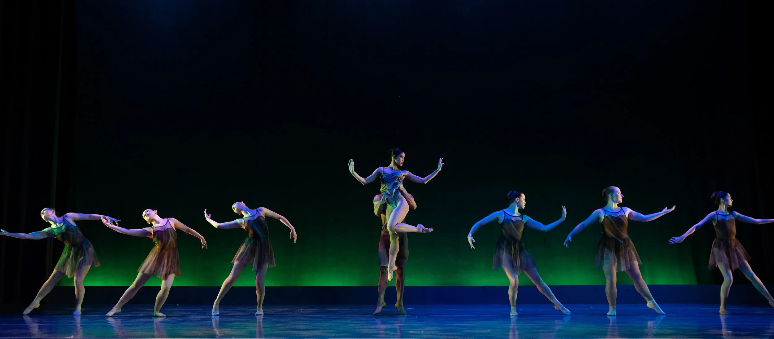 Ballet dancers perform on stage under stage lighting with a dark background.