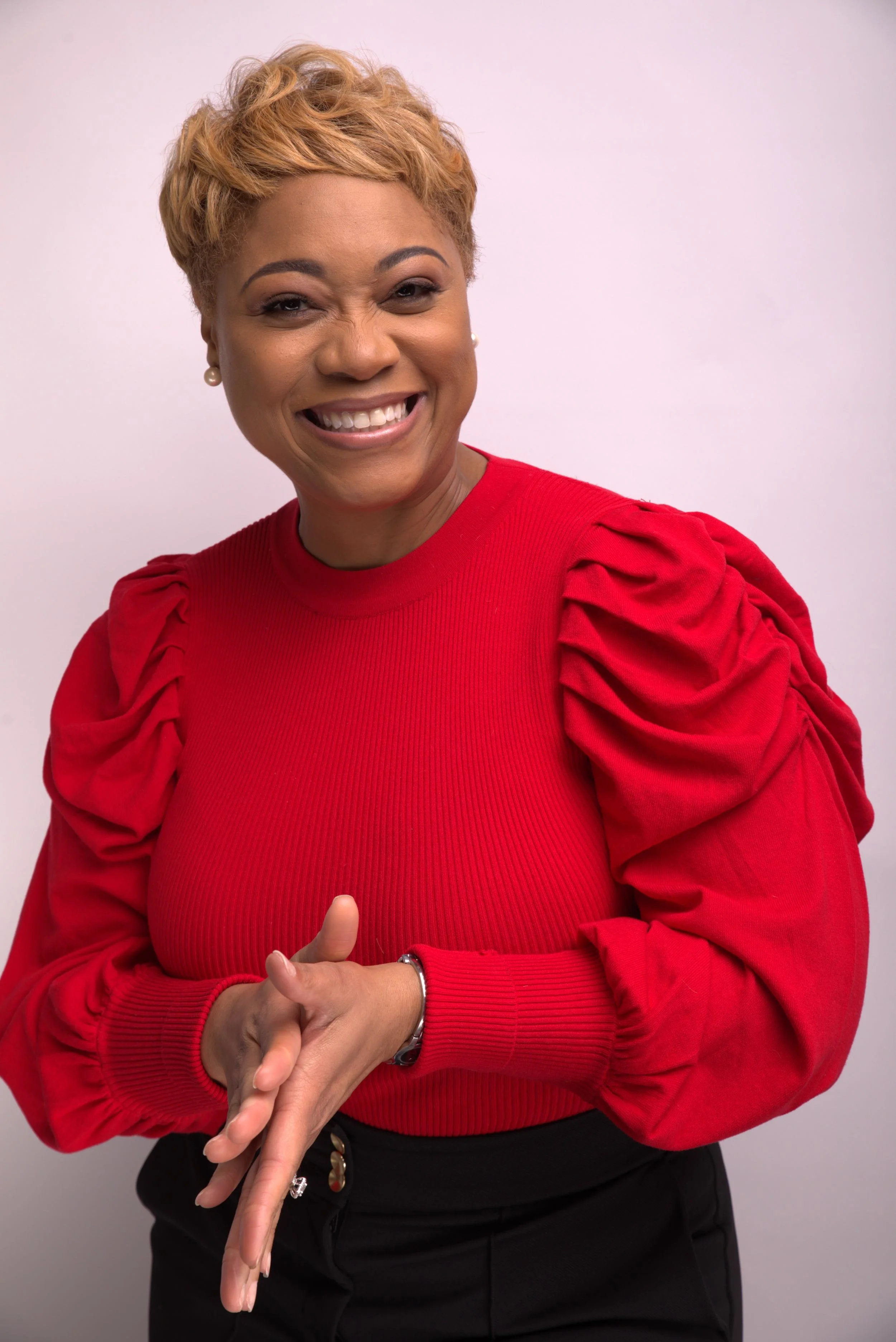 A woman smiling and wearing a red top with puffed sleeves, standing against a light background.