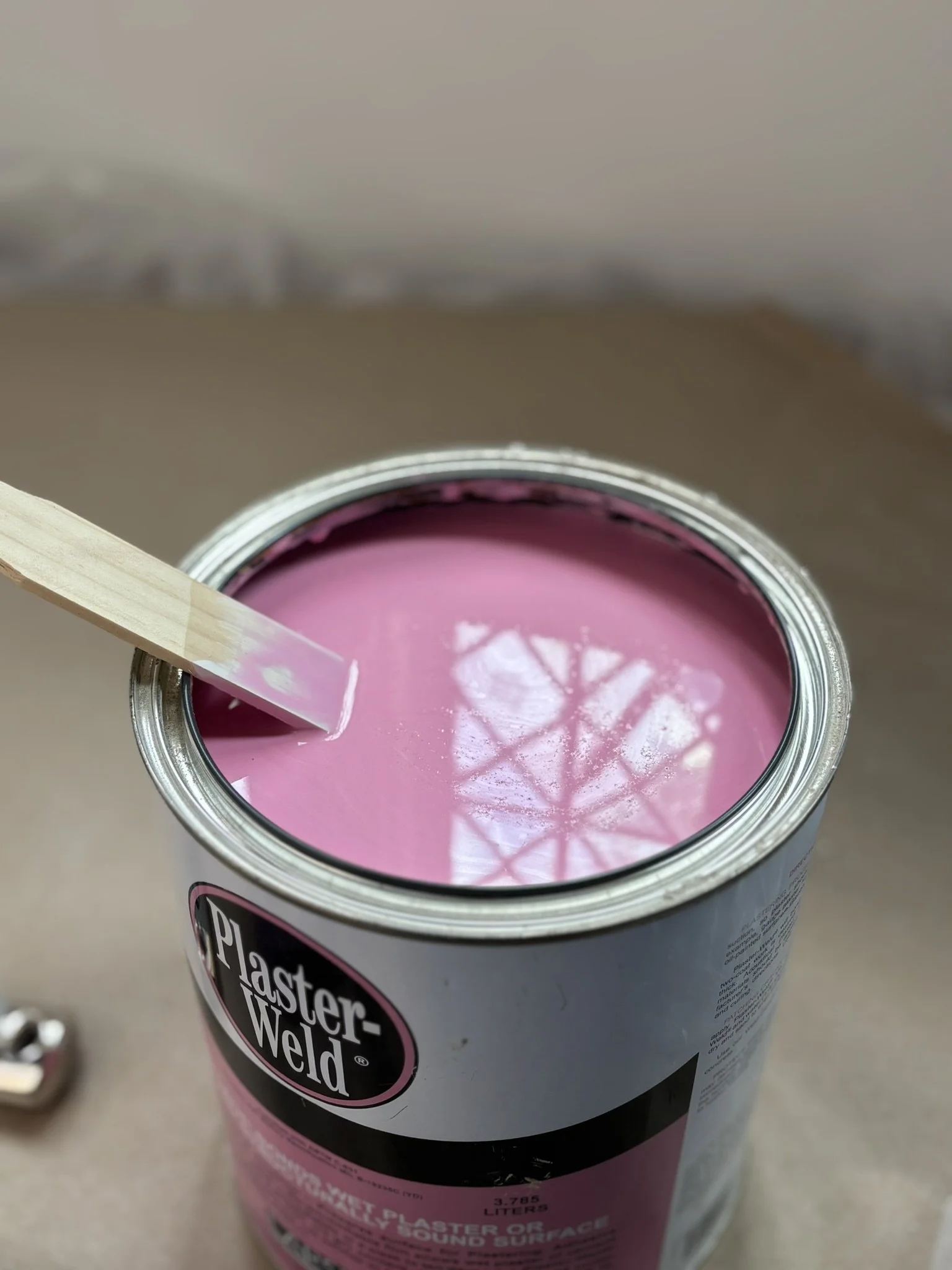 A can of pink Plaster-Weld with the lid partially removed and a tongue depressor being dipped into the pink substance.