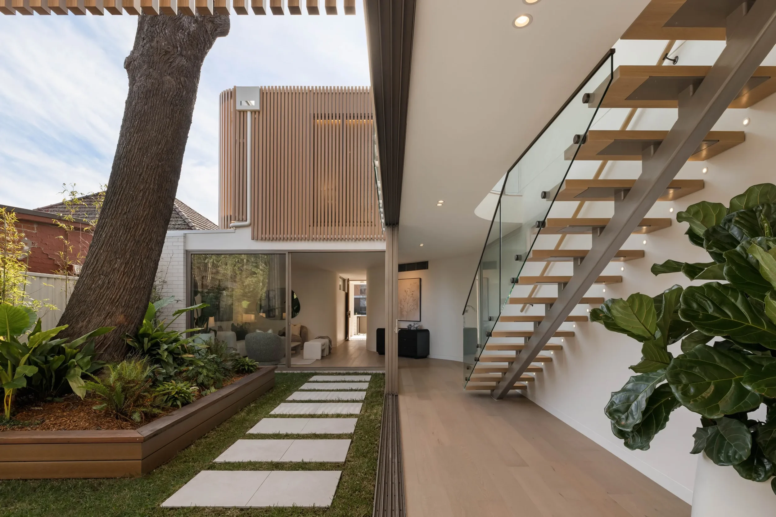 Modern house with outdoor area, glass staircase, plants, and a tree in the foreground.