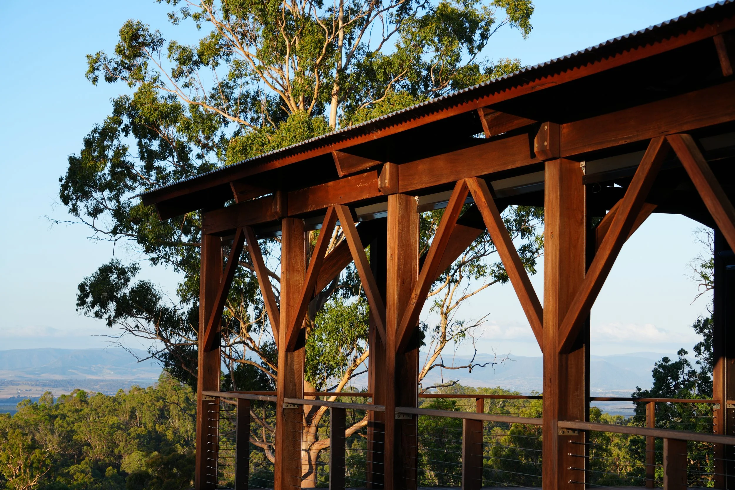 An open air chapel railing overlooking a green landscape and trees, under a clear blue sky.