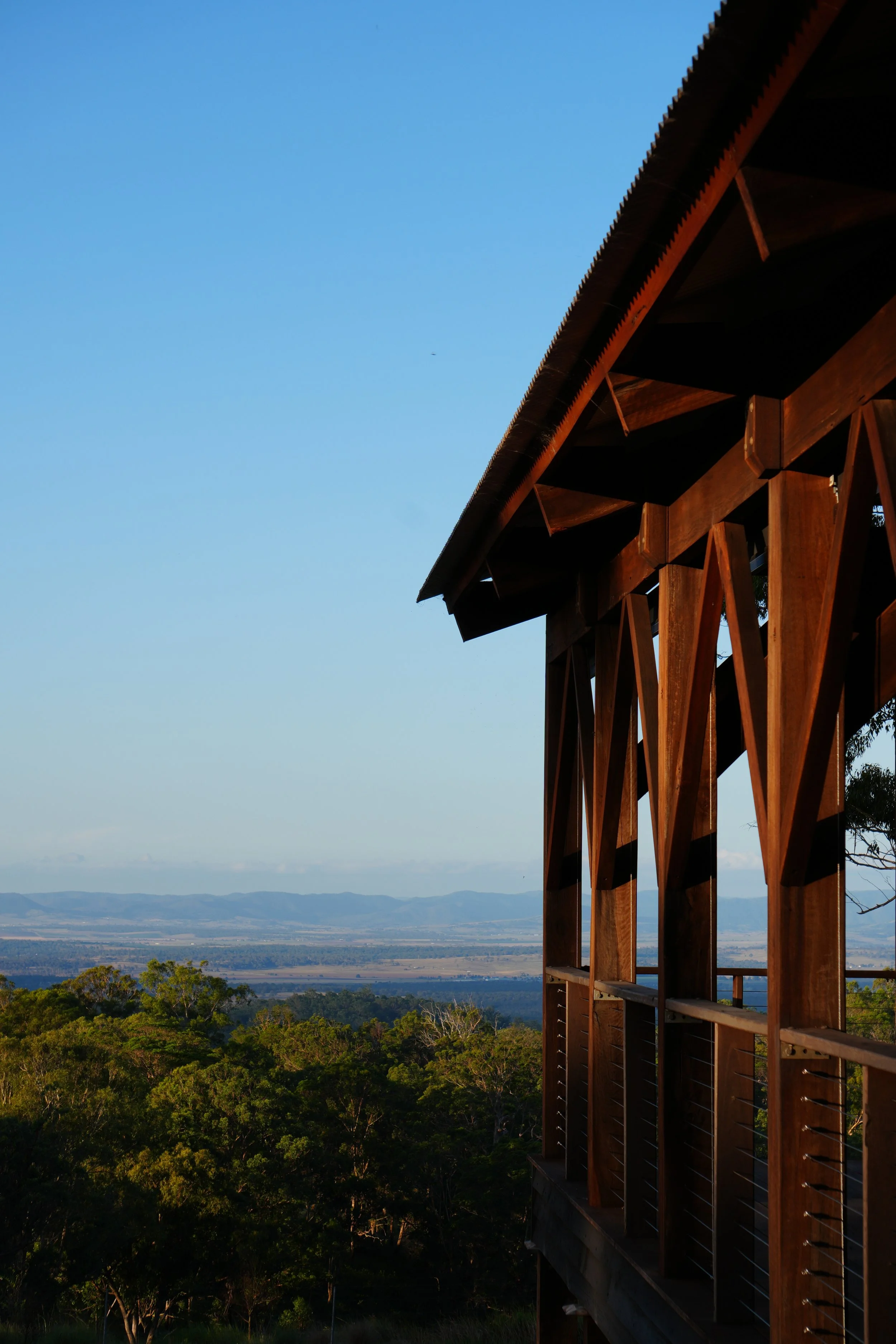 A open air chapel overlooking landscape with trees, fields, and mountains in the distance under a clear blue sky.