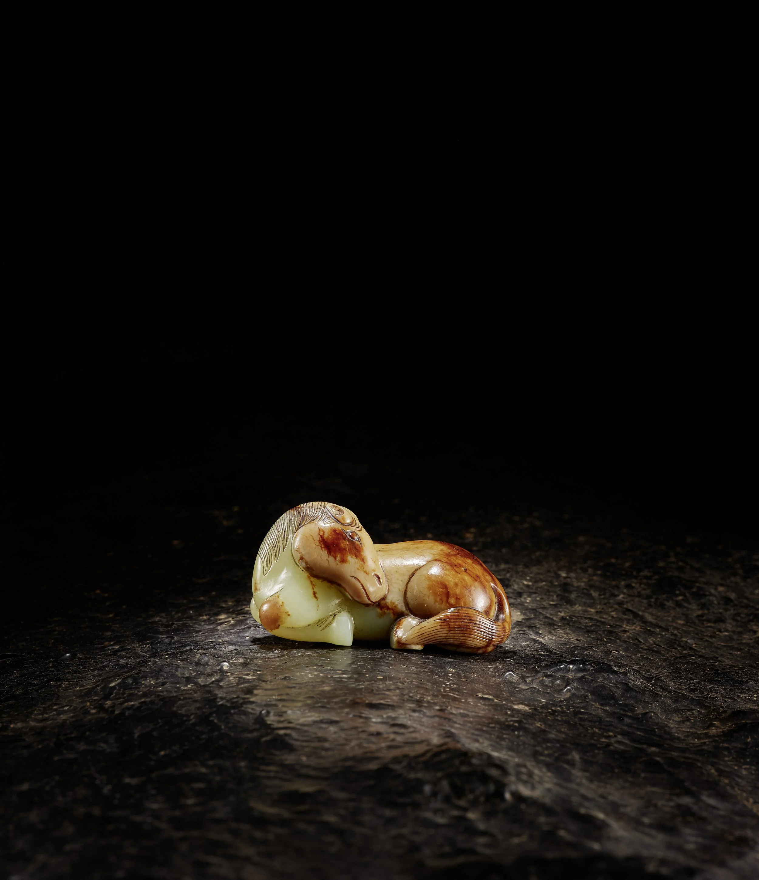 A yellow, caramel and deep russet jade model of a recumbent horse, colours to the head and rest of the body,
China: Ming dynasty (1368–1644), wood stand